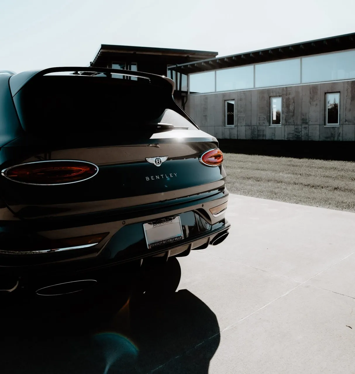 Rear of a black Bentley SUV parked outside a modern concrete home