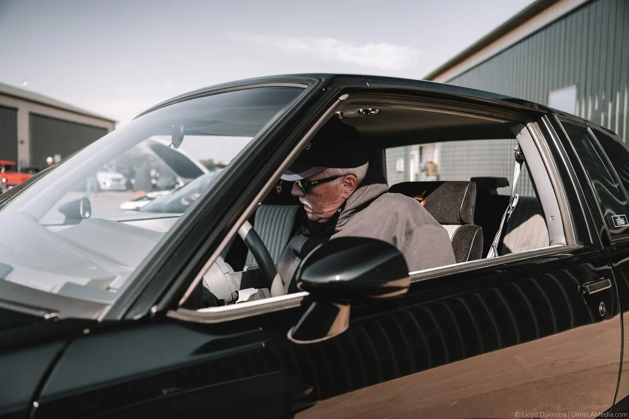 Older owner seated in his black Buick Grand National at a show
