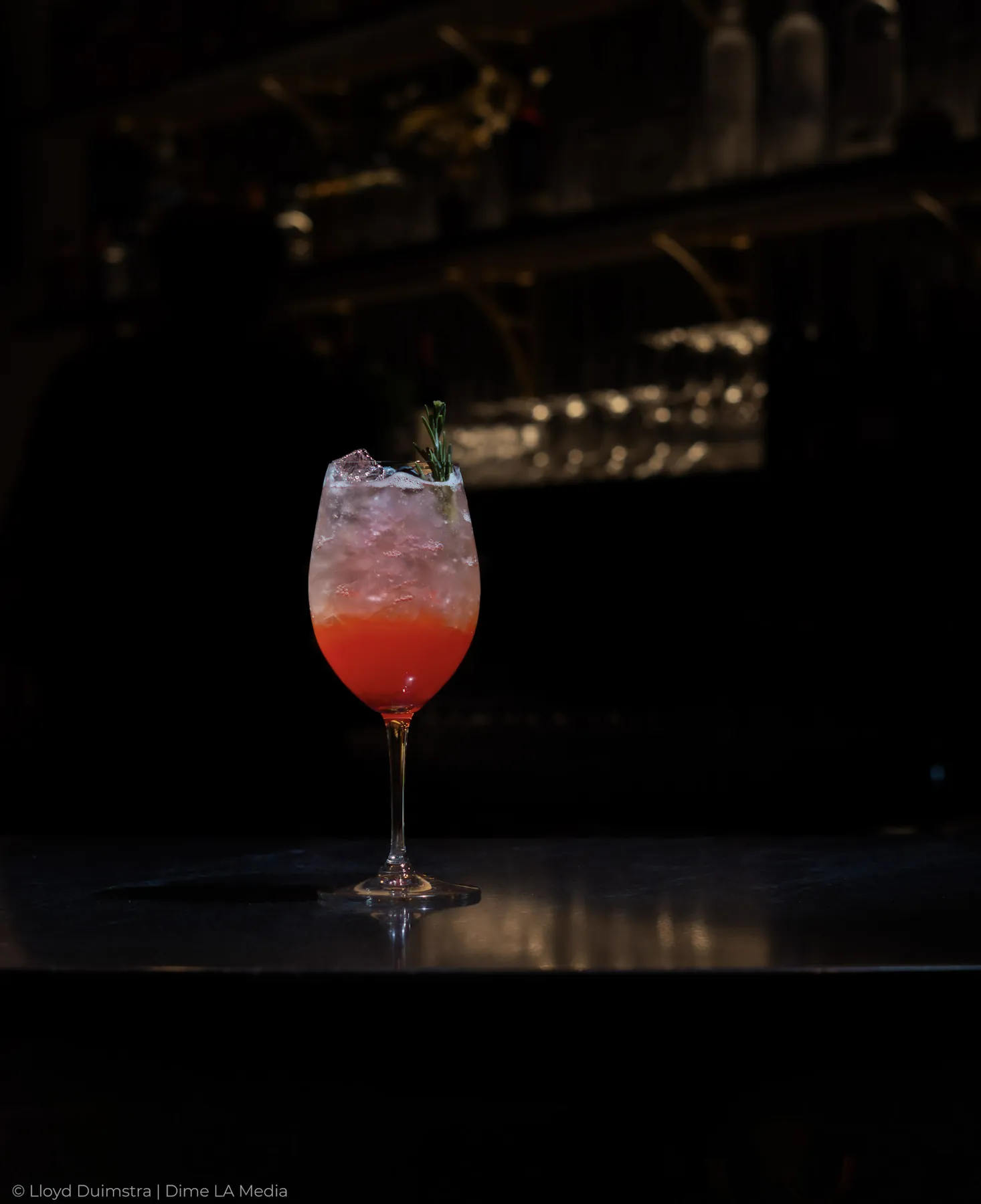 Red ombre wine-glass cocktail with rosemary in a moody bar