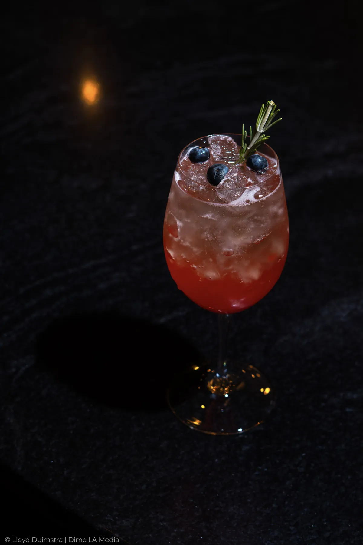 Berry spritz in a wine glass with blueberries and rosemary on black stone
