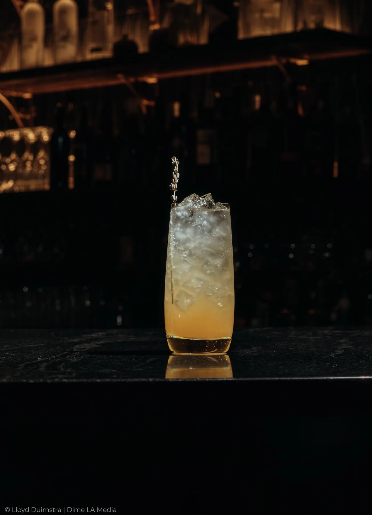 Golden highball cocktail with a lavender sprig against a warm back bar
