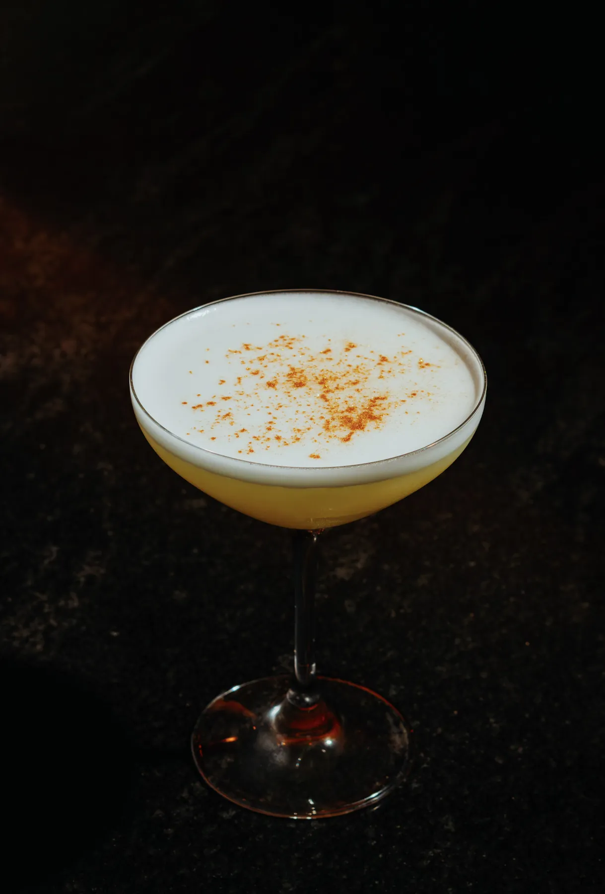 Whiskey sour in a coupe with a foam top dusted with cinnamon