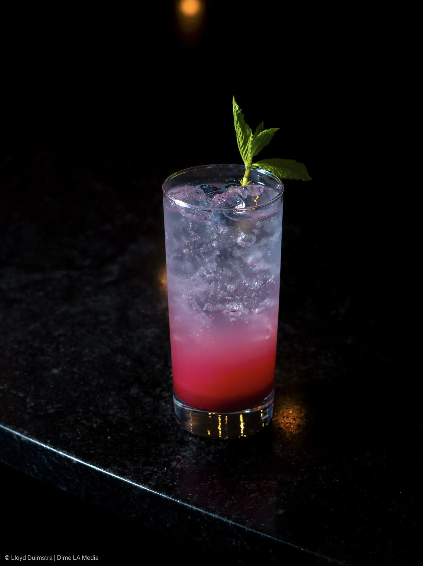 Berry ombre highball with fresh mint on black stone, backlit