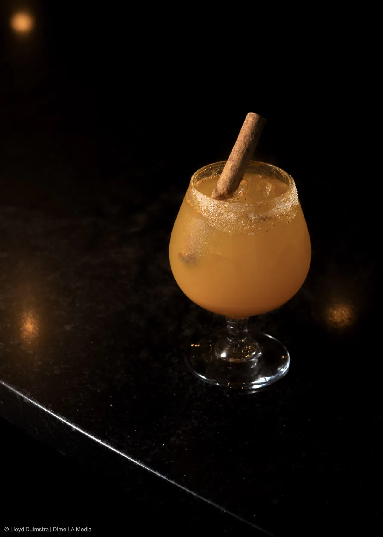 Spiced amber cocktail with a cinnamon stick and sugared rim on a dark bar