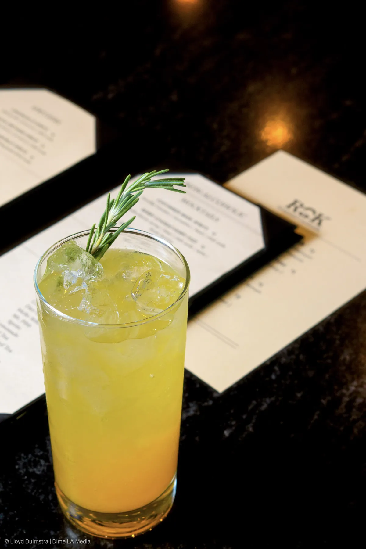 Bright citrus highball with a rosemary sprig beside a cocktail menu