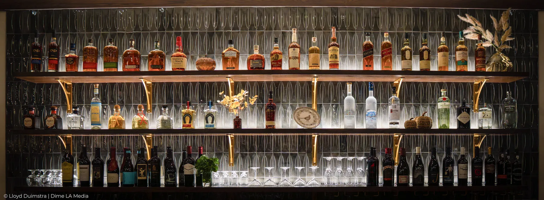 Fully stocked back bar shelf of whiskey, gin and wine bottles under warm light