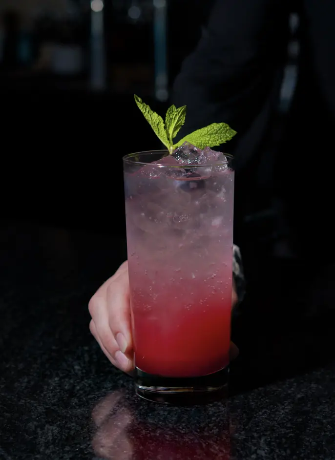 Tall pink ombre cocktail garnished with mint, held on a dark bar top, Rivage Oak Kitchen, Sioux Falls SD