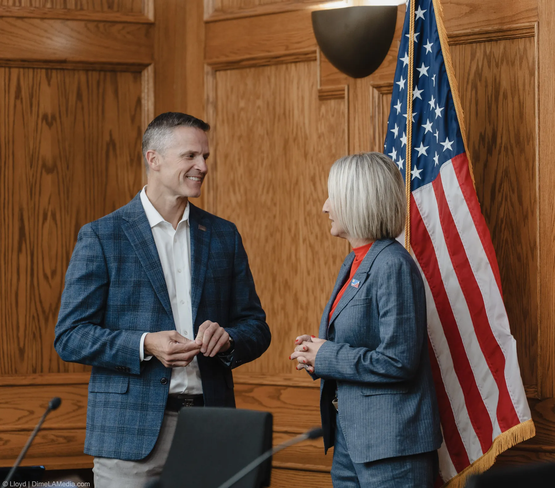 Outgoing mayor Paul TenHaken talks with mayor-elect Christine Erickson beside the American flag at Carnegie Town Hall