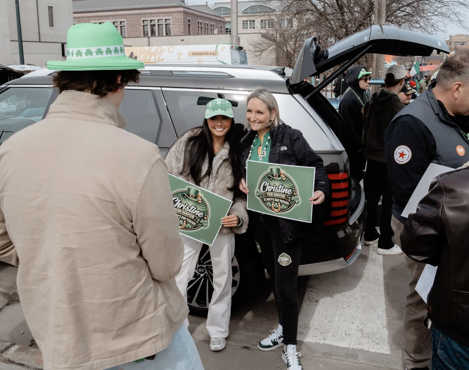 Campaign volunteers in green gather with signs before the St. Patrick's Day parade in Sioux Falls