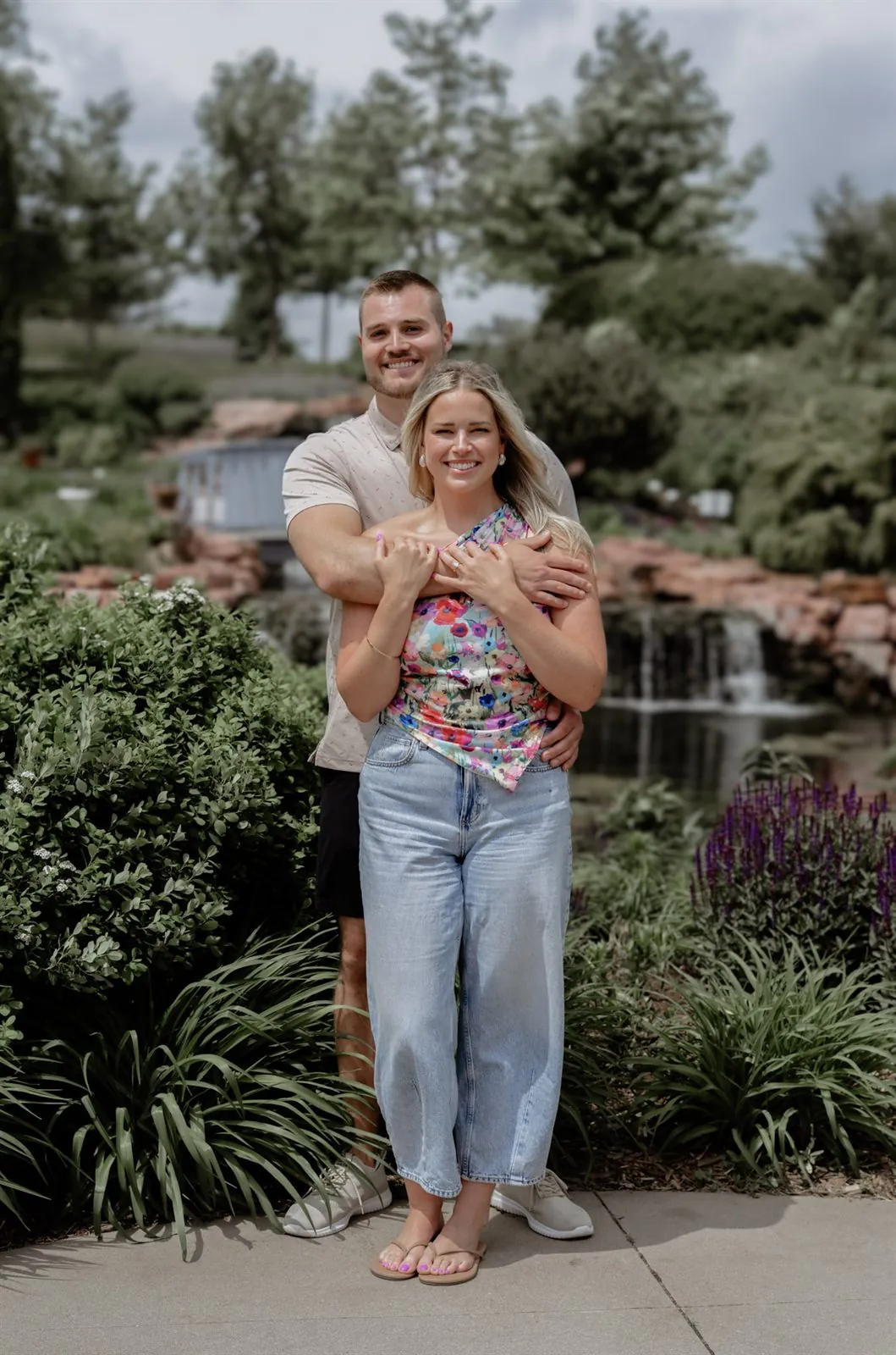 Man embracing his fiancee from behind as both smile in a garden