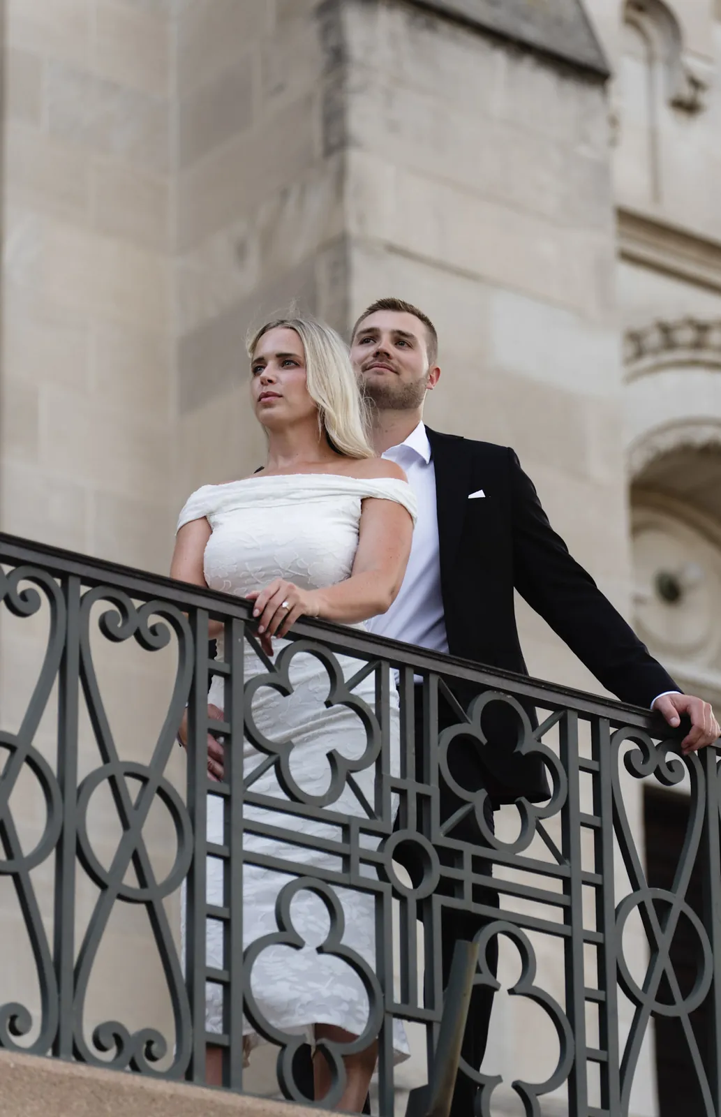 Engaged couple gazing out over a wrought-iron railing at the cathedral