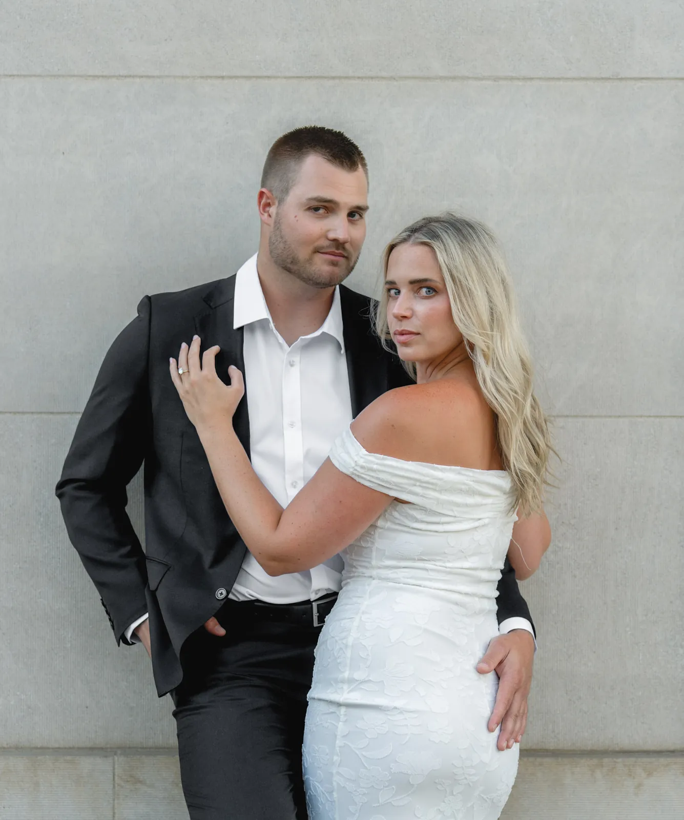 Editorial engagement portrait of a couple in a black suit and white dress against limestone, downtown Sioux Falls SD