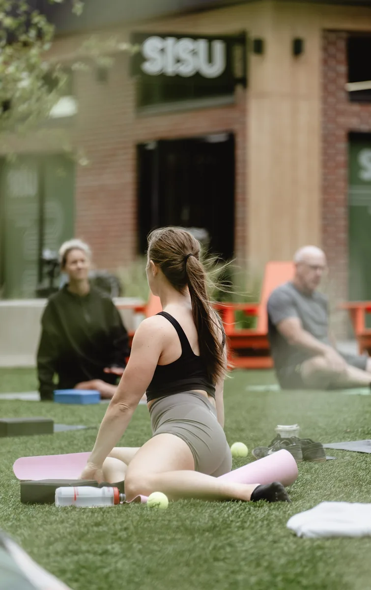 A participant holding a seated position on the lawn outside Sisu during the outdoor Kinstretch class, Sioux Falls SD
