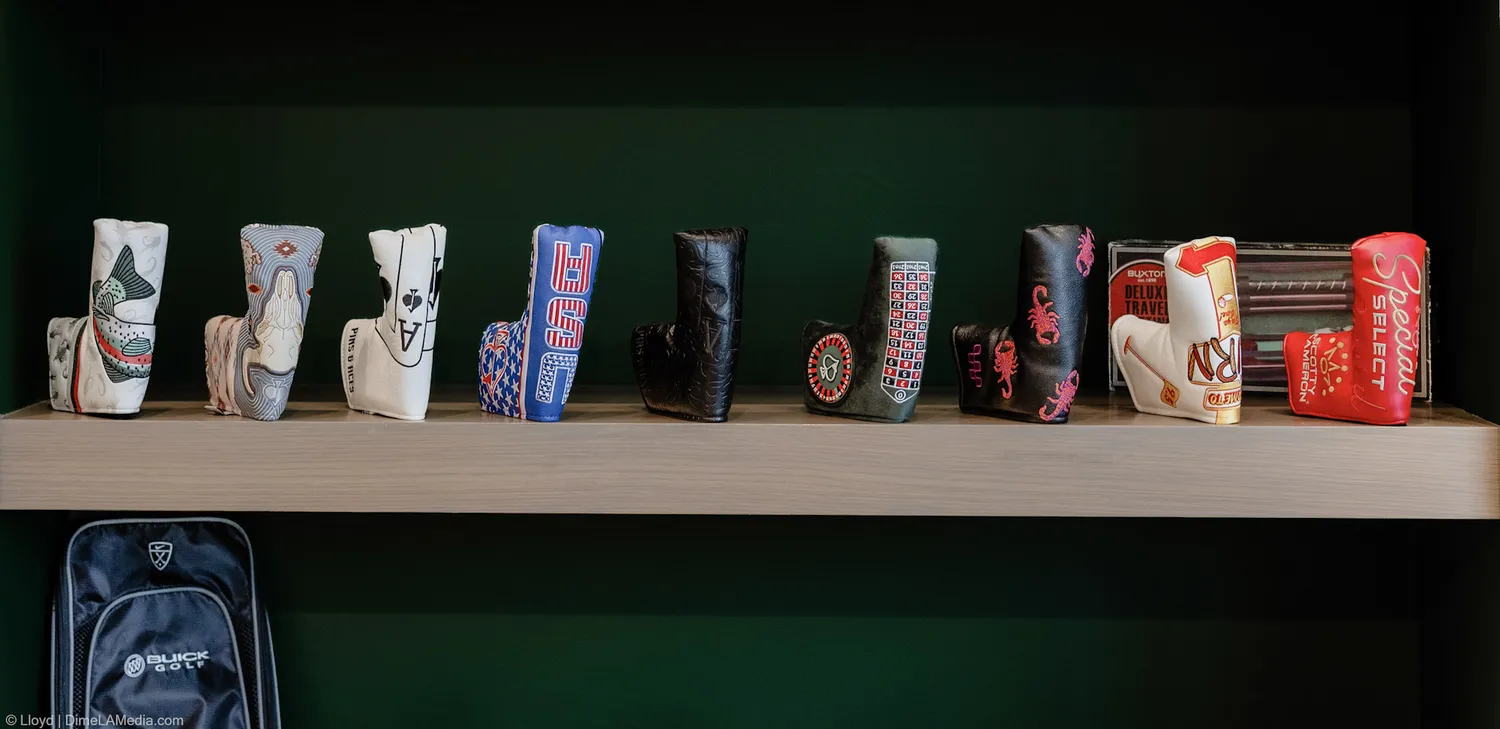 A long shelf of golf headcovers photographed against the green wall at Final Drive