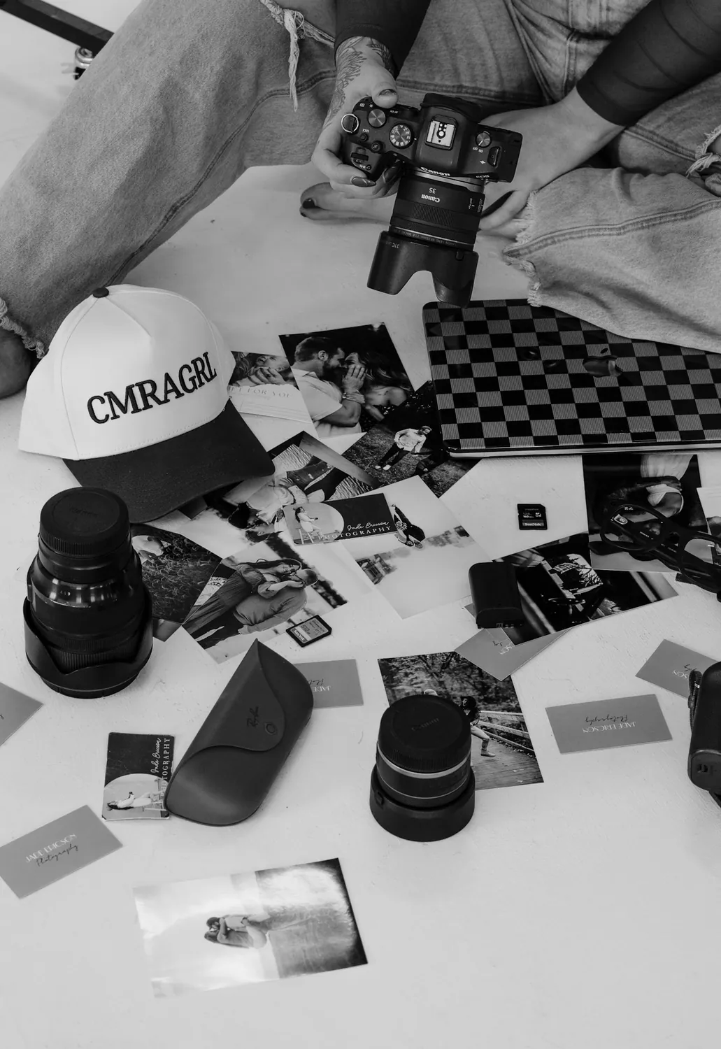 Black and white flat lay of Jade's cameras, prints, and laptop on the studio floor