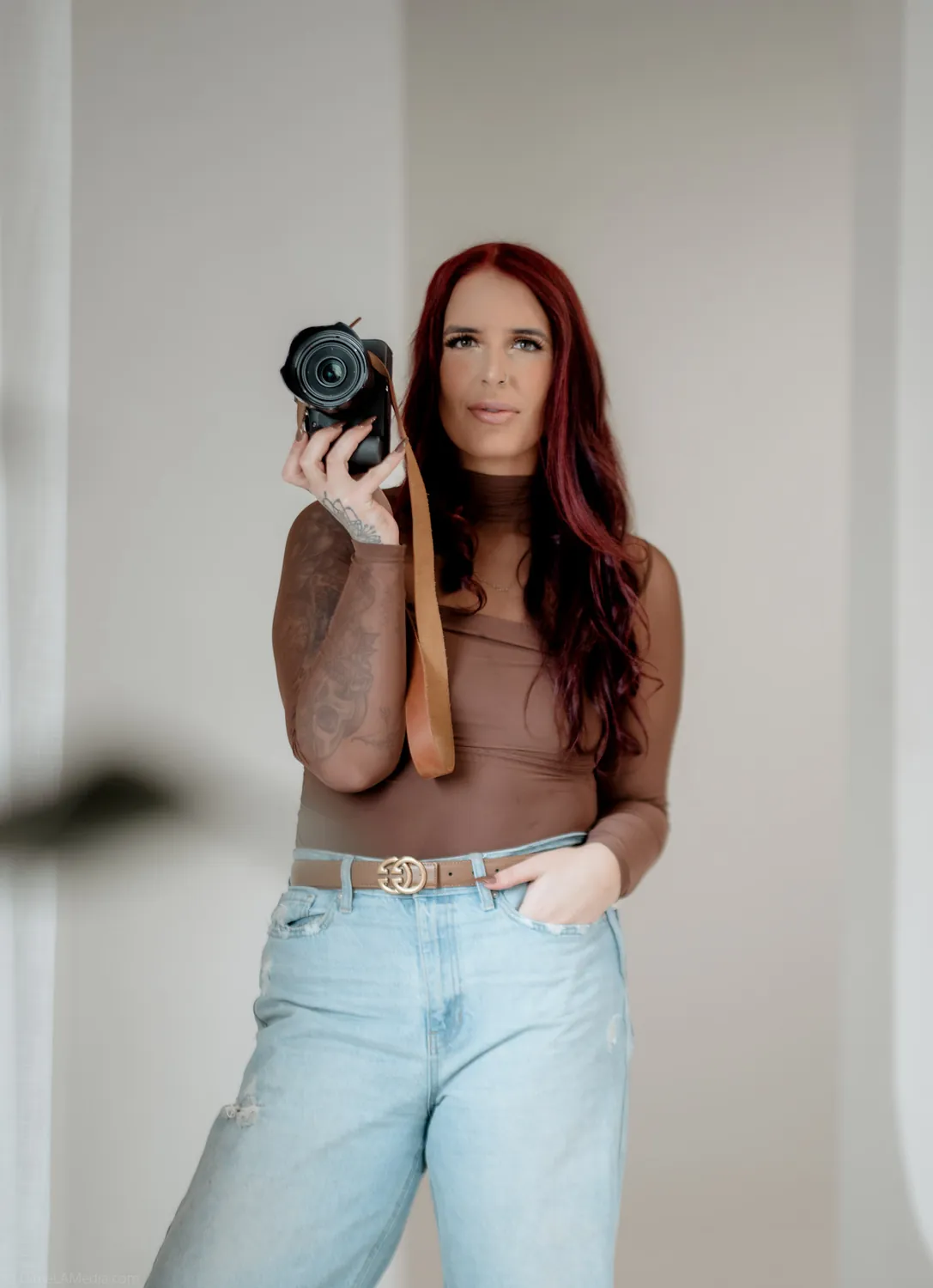 Jade holds her camera at eye level in soft window light during her personal brand session
