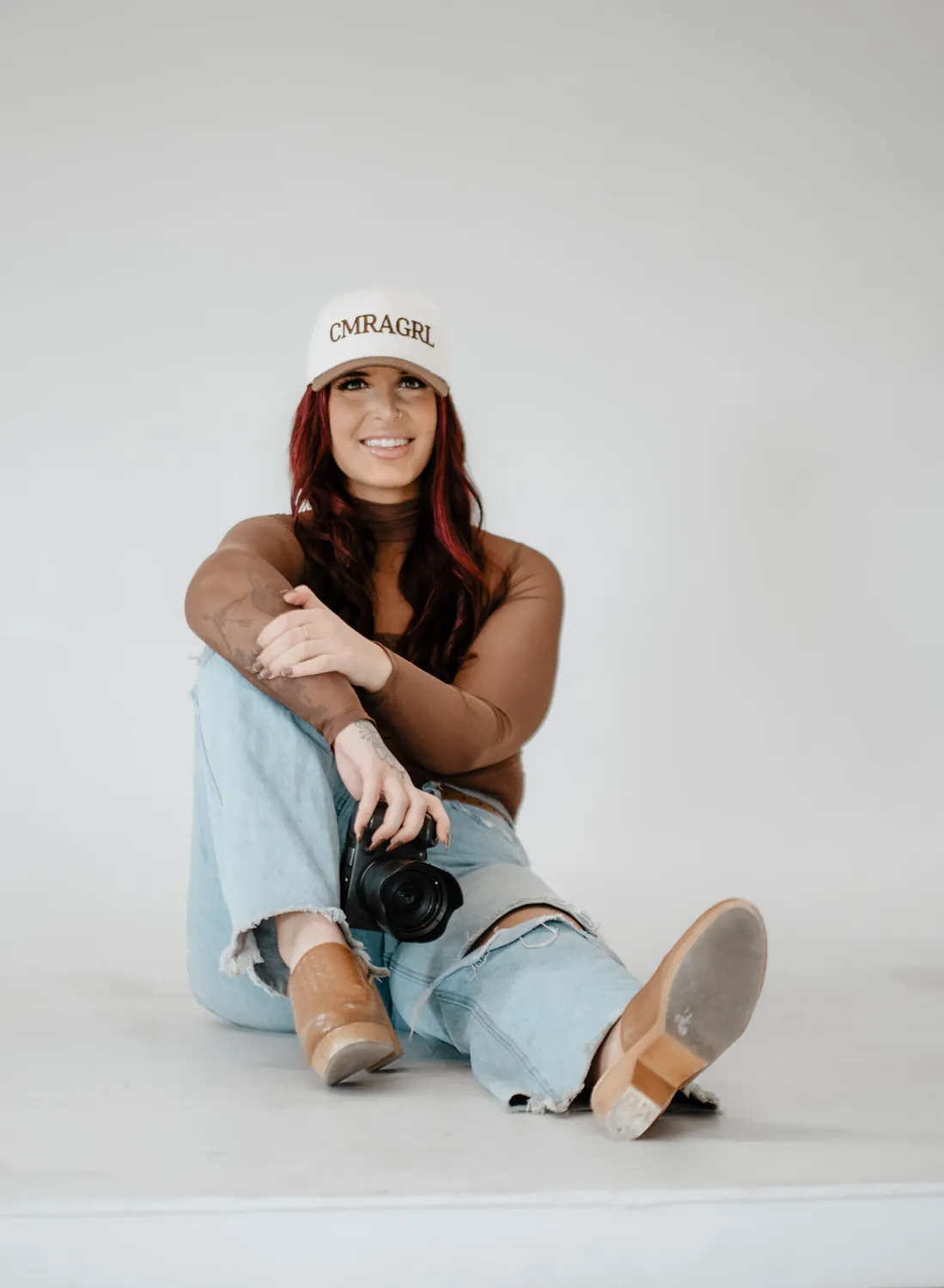Jade sits on the studio floor holding her camera during a personal brand photography session