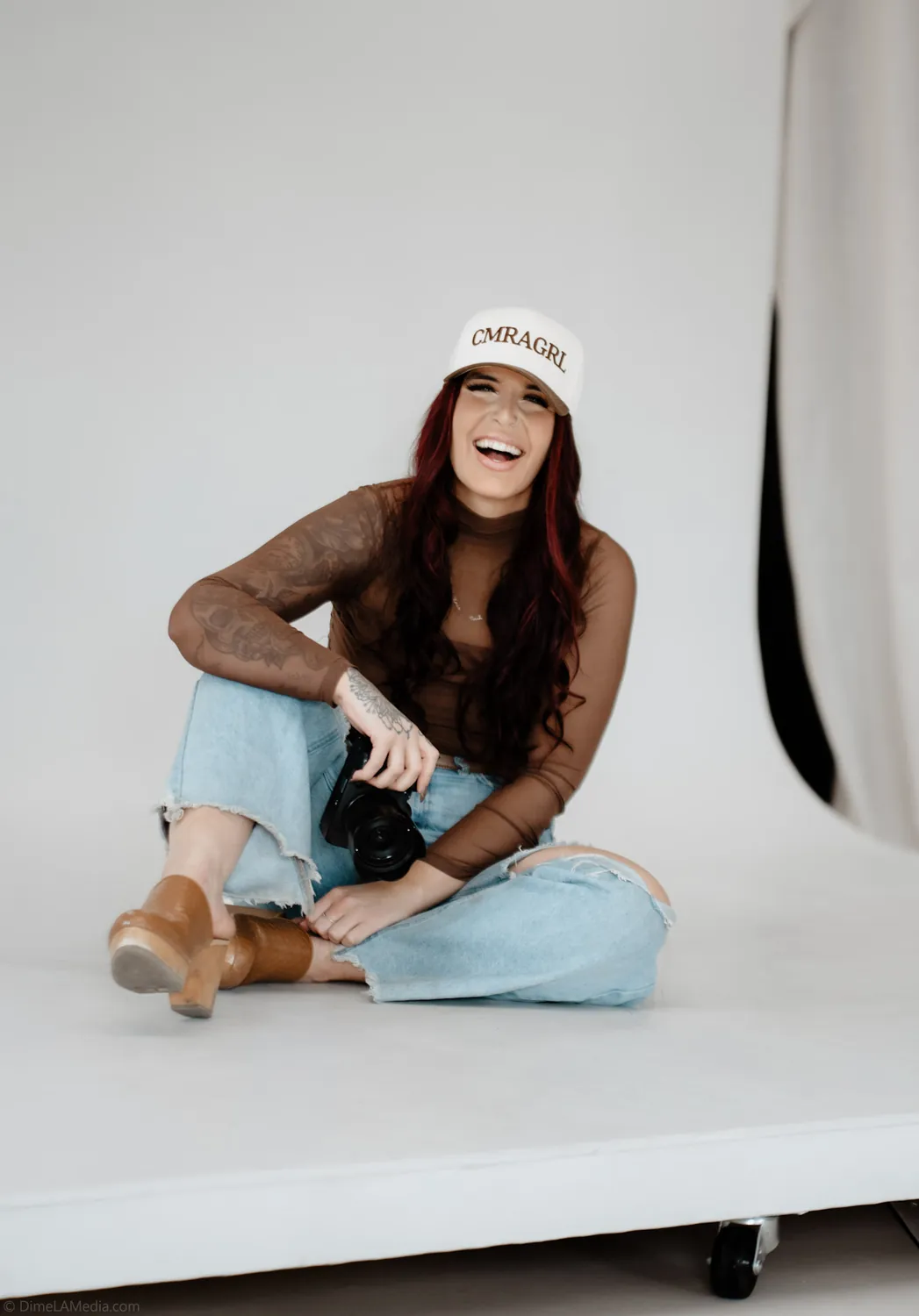 Jade laughs on the white studio backdrop holding her camera