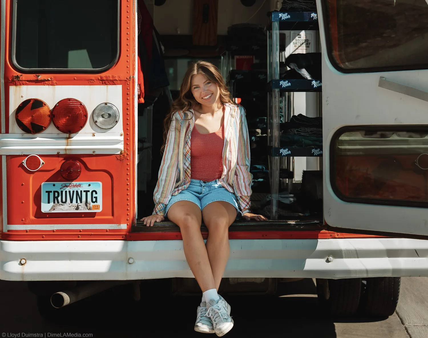 Maddie Theisen sits on the open tailgate of the True Vintage bus above the TRUVNTG license plate