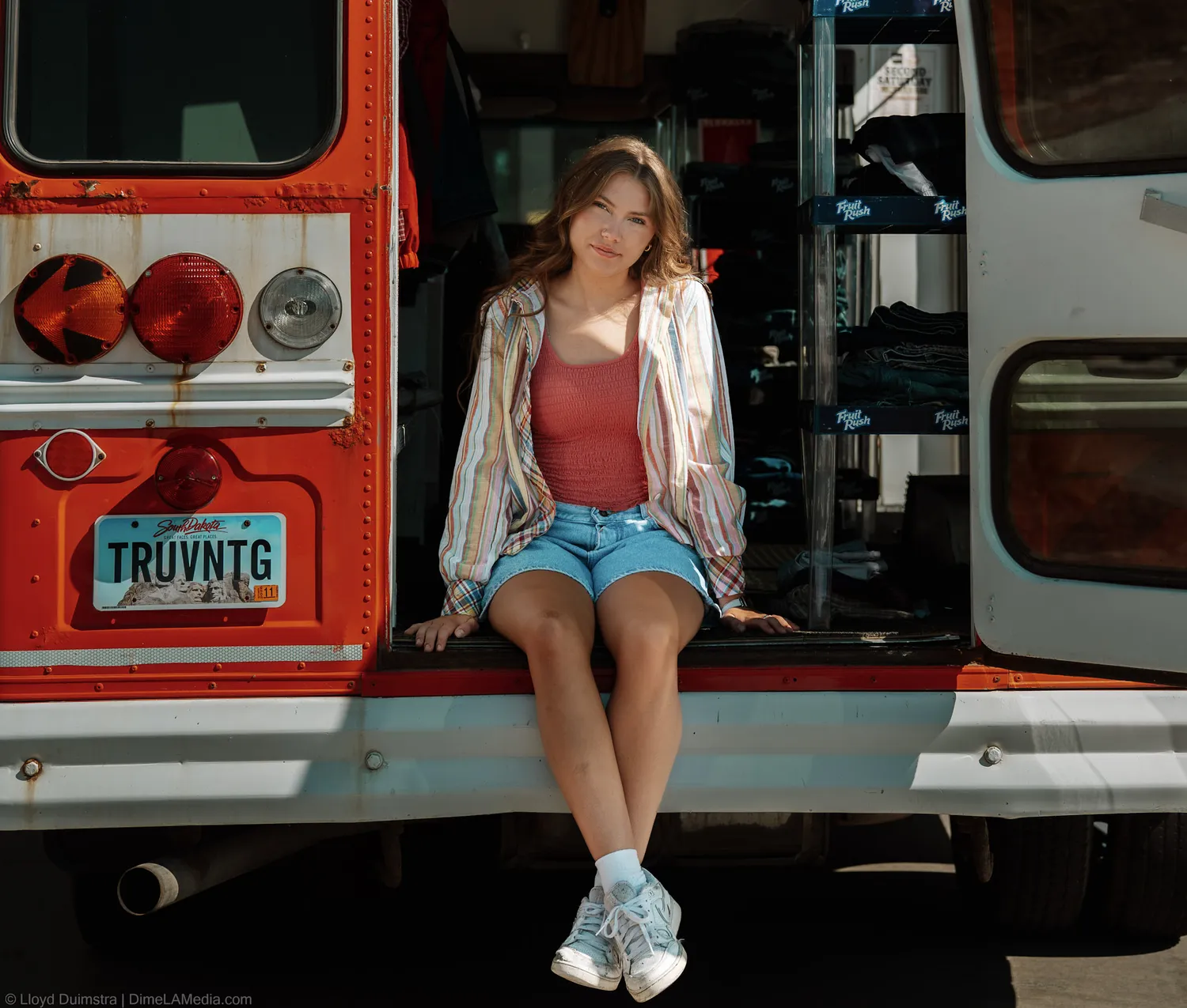 Maddie Theisen seated on the True Vintage bus tailgate with clothing racks visible inside