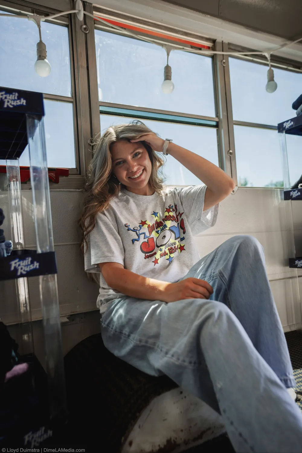 Maddie Theisen in a white graphic tee sits by the windows of the True Vintage bus
