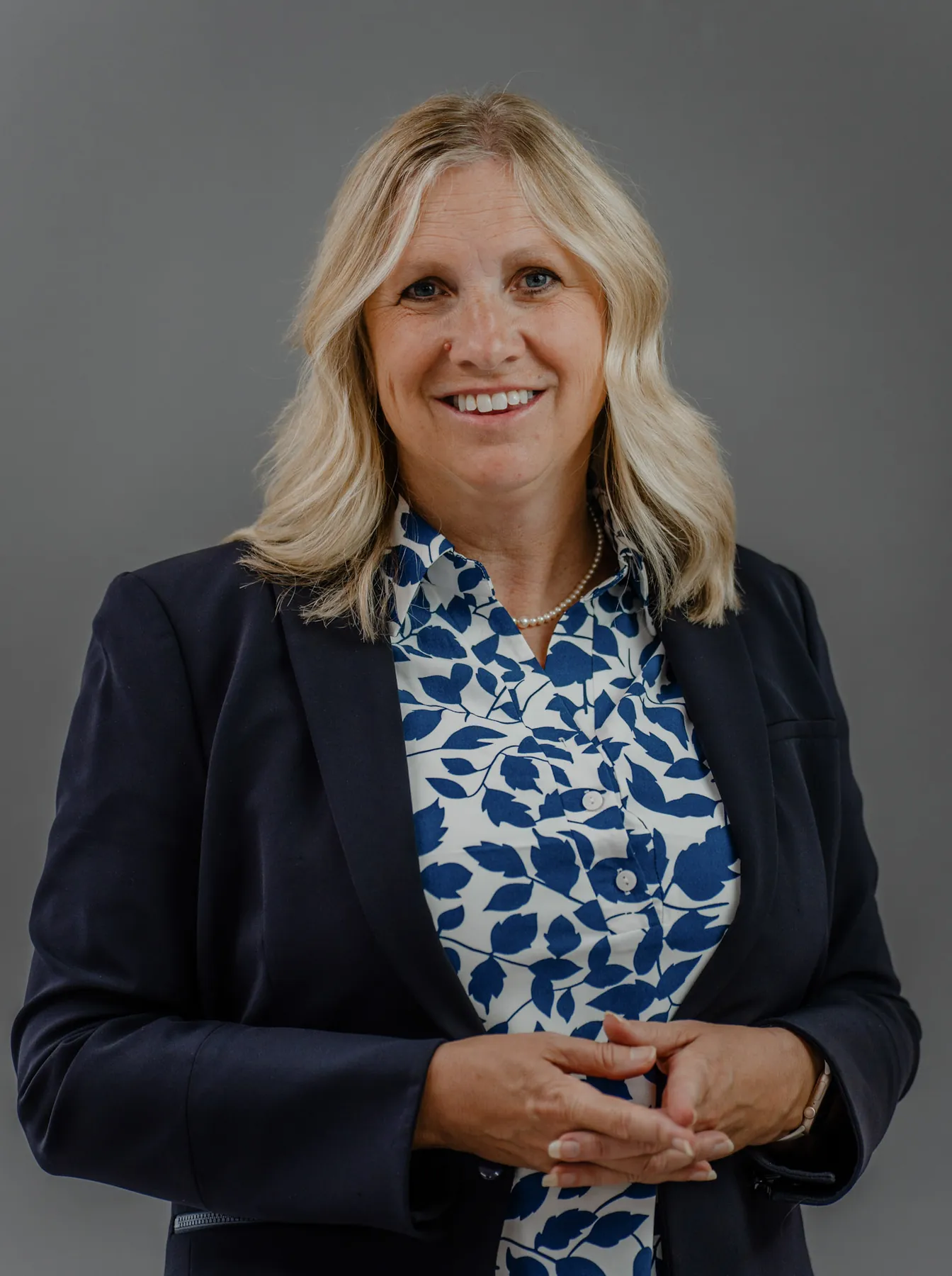 Corporate headshot of a woman in a navy blazer on a grey studio backdrop, Sioux Falls SD
