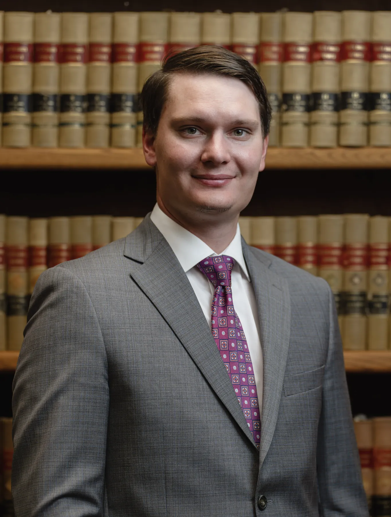 Attorney headshot in a gray suit in front of law books