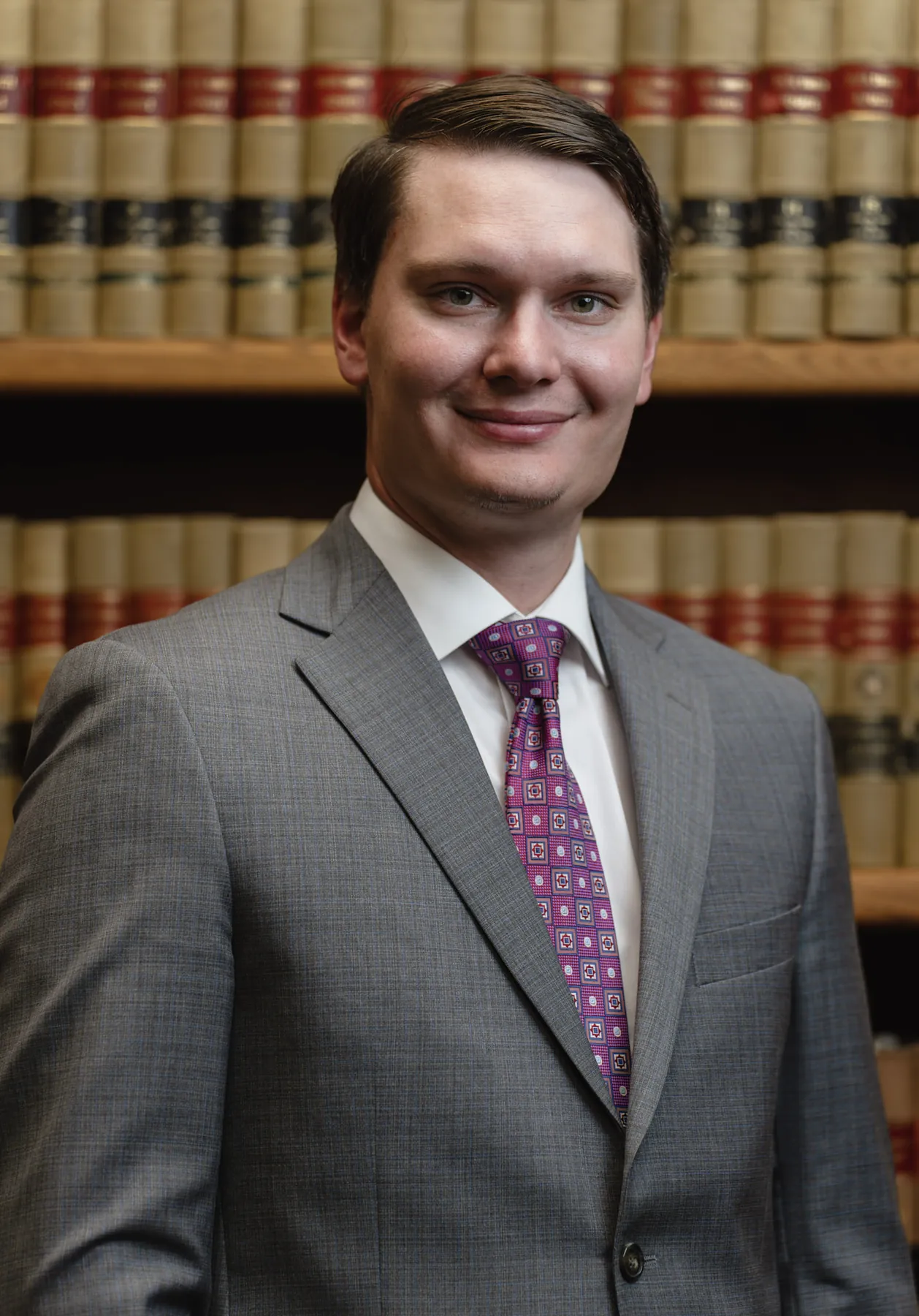 Smiling attorney headshot in a gray suit, law office library