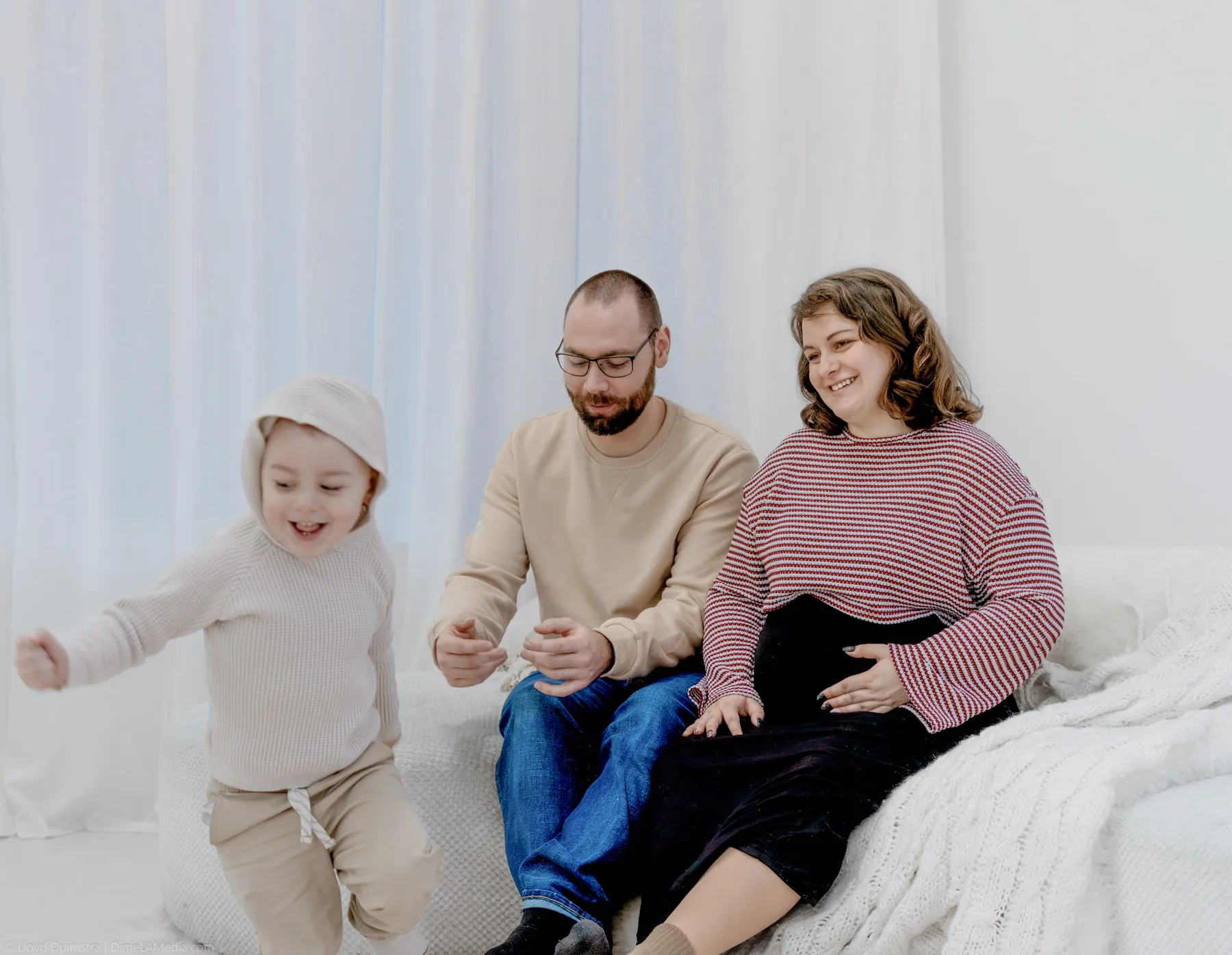 Toddler toddling along the studio couch beside mom and dad