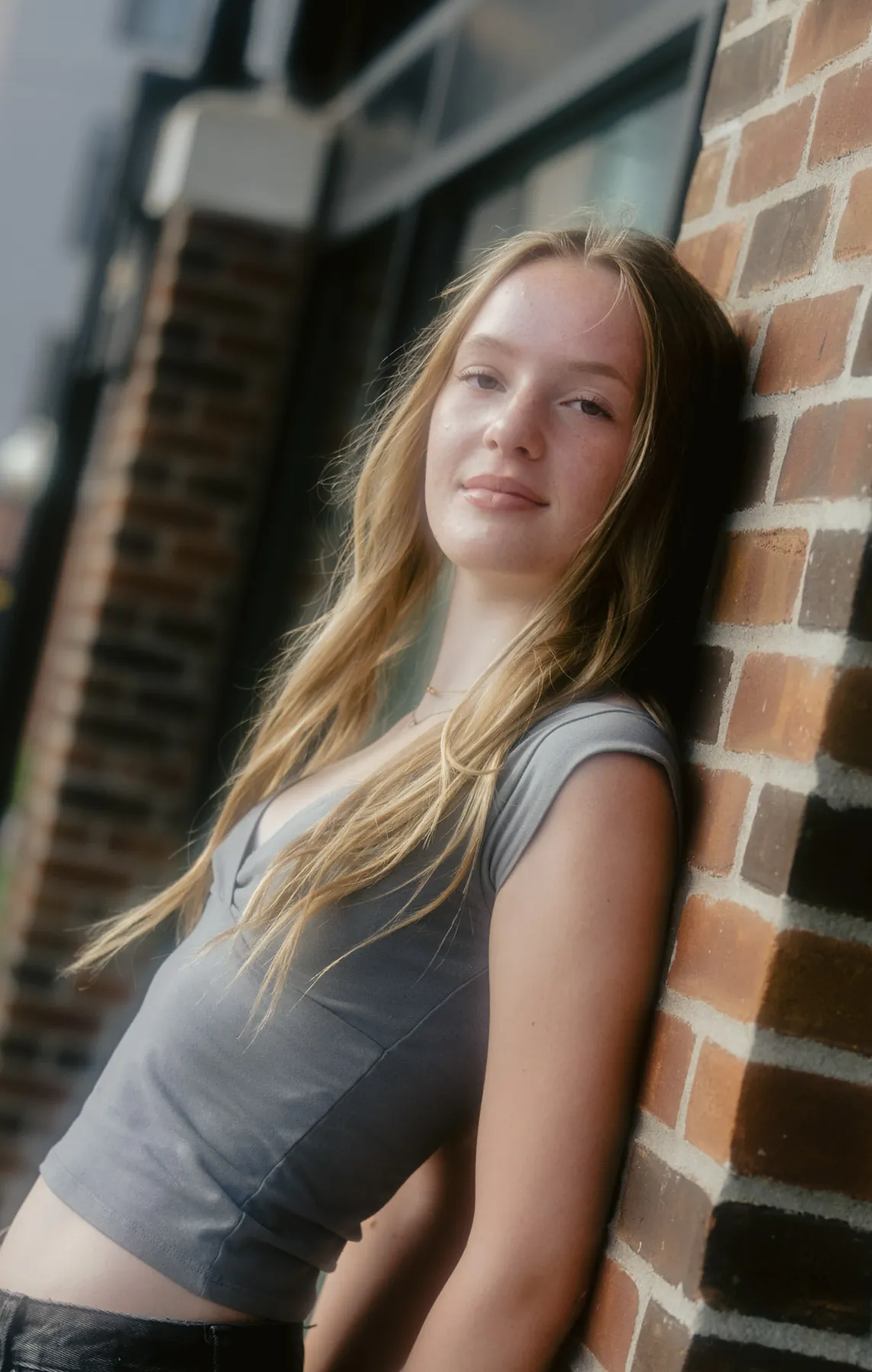 Scout looking to camera against a warm brick wall, film-toned senior portrait