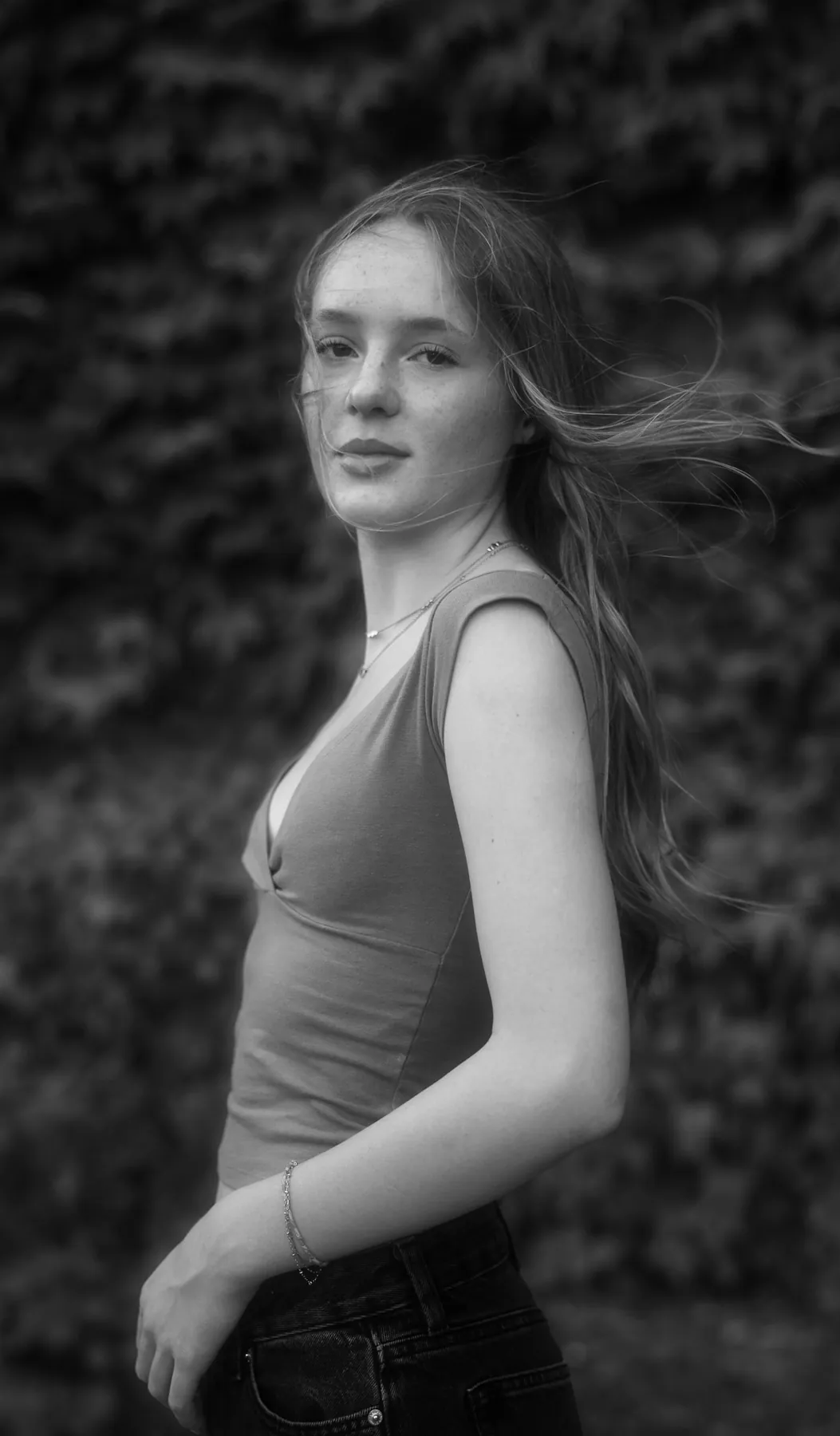 Black and white senior portrait of Scout with her hair caught in the wind against dark ivy