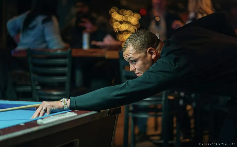 Pool player stretching across the table under bar light