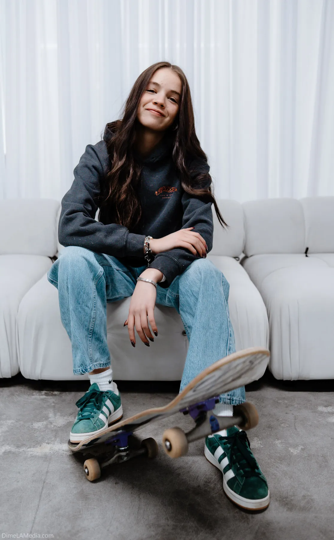 Creative portrait of a woman seated with a skateboard on a white couch