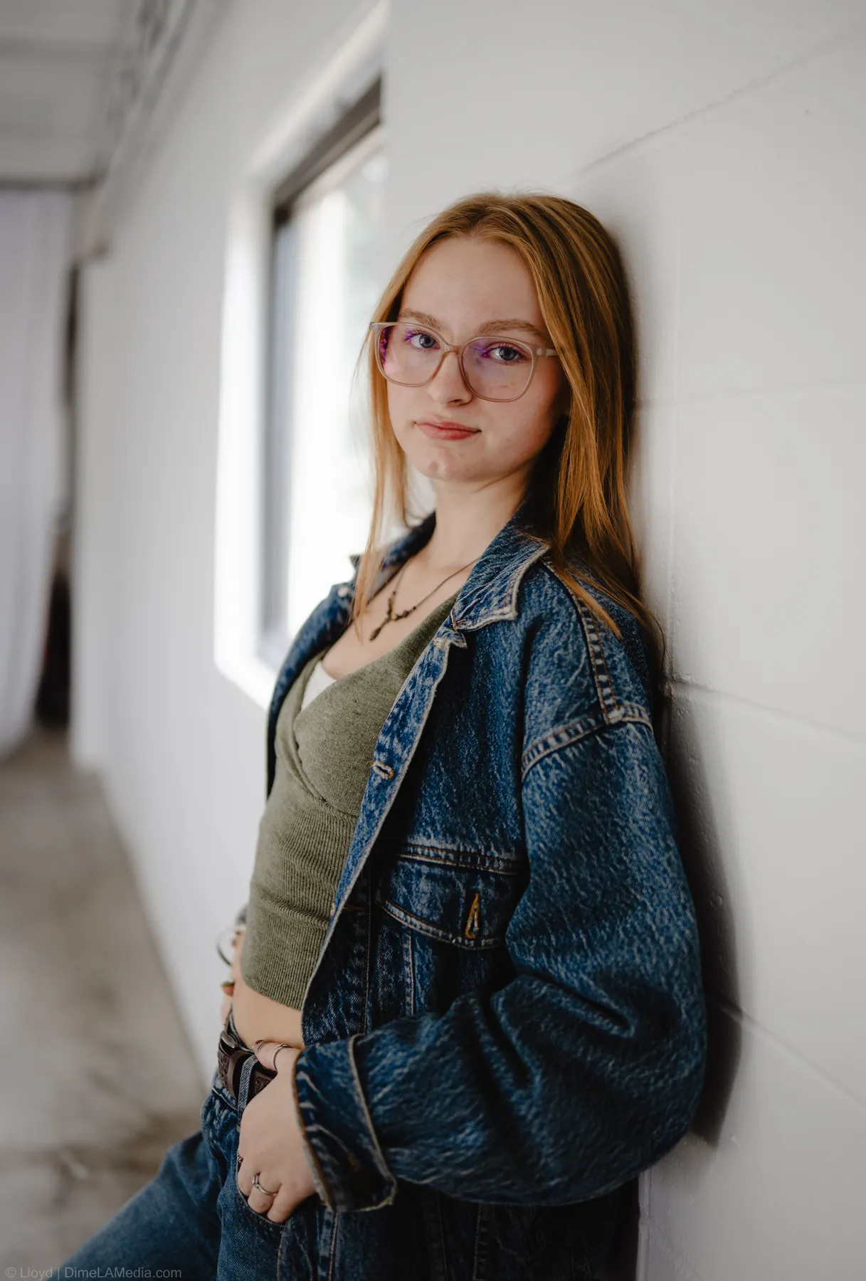 Syd Patzwald in a denim jacket leaning against a wall beside a window, studio portrait