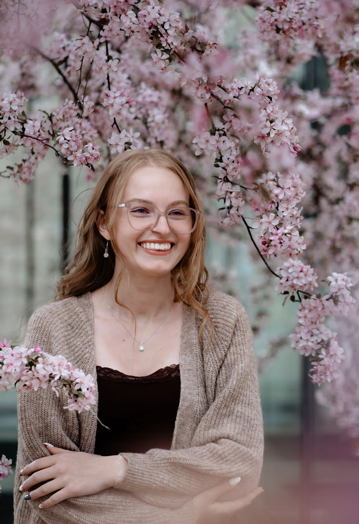 Syd Patzwald smiling in a knit cardigan among crabapple blossoms