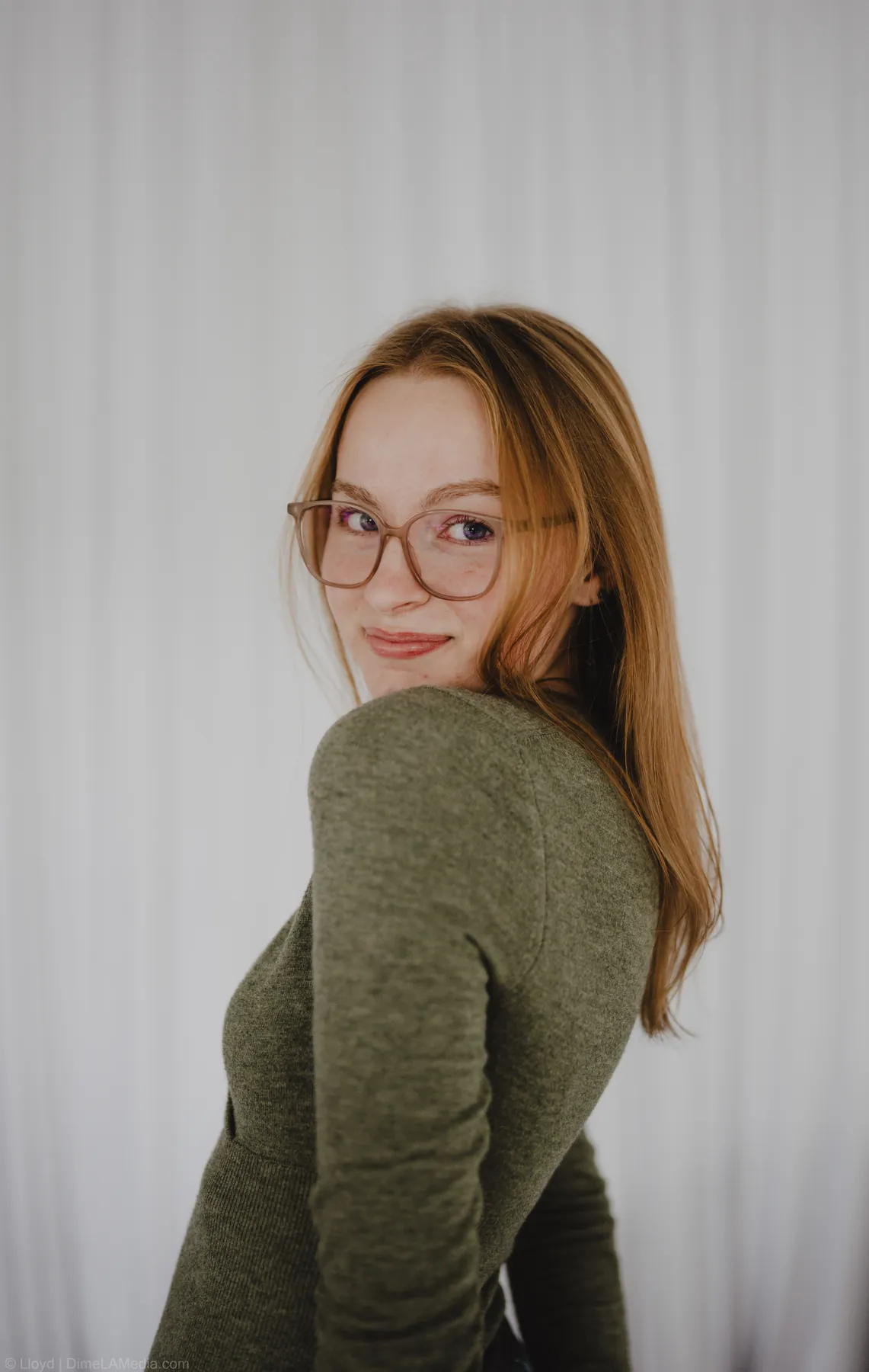 Syd Patzwald glancing over her shoulder in an olive sweater, studio portrait