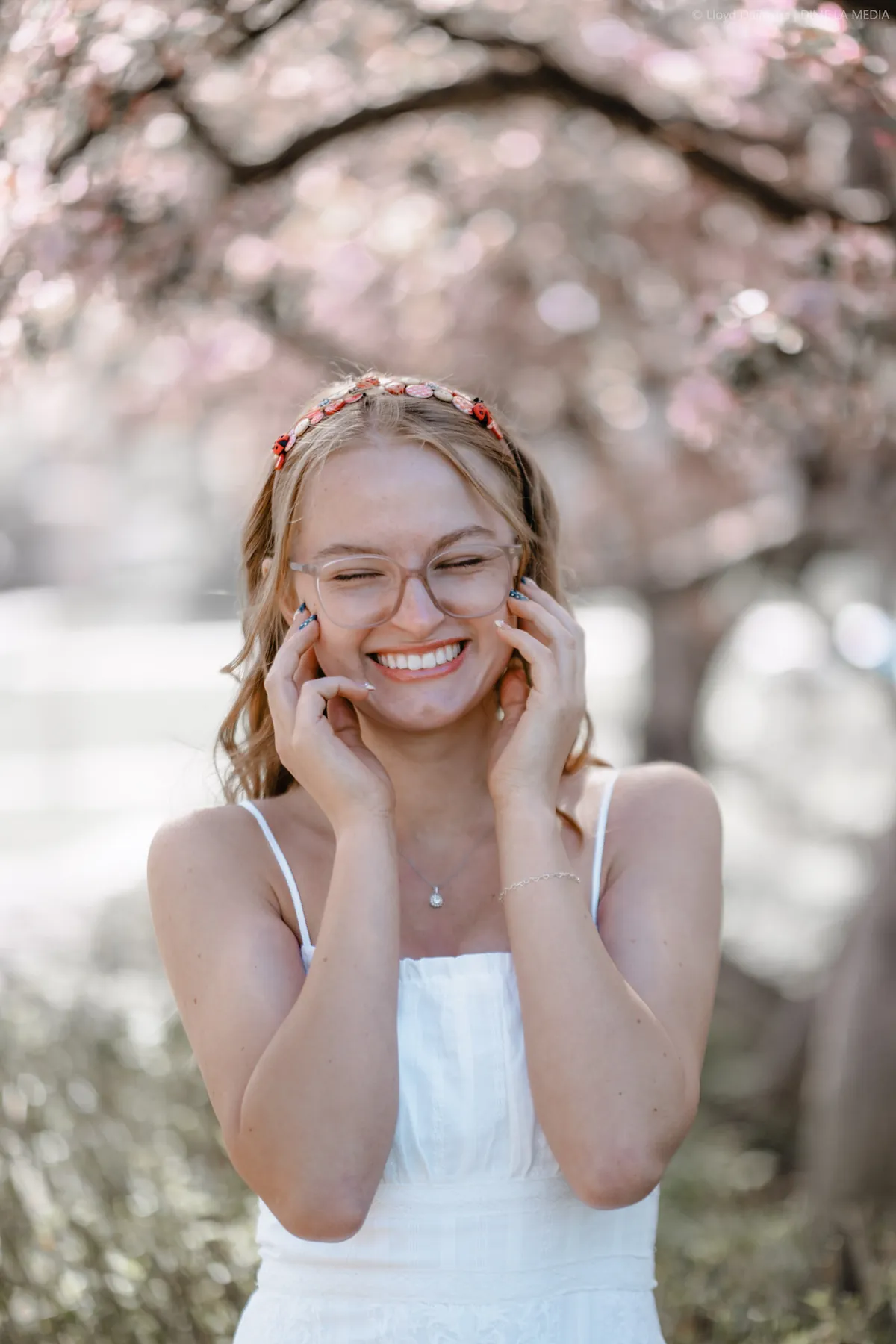 Syd Patzwald smiling in a white dress under crabapple blossoms