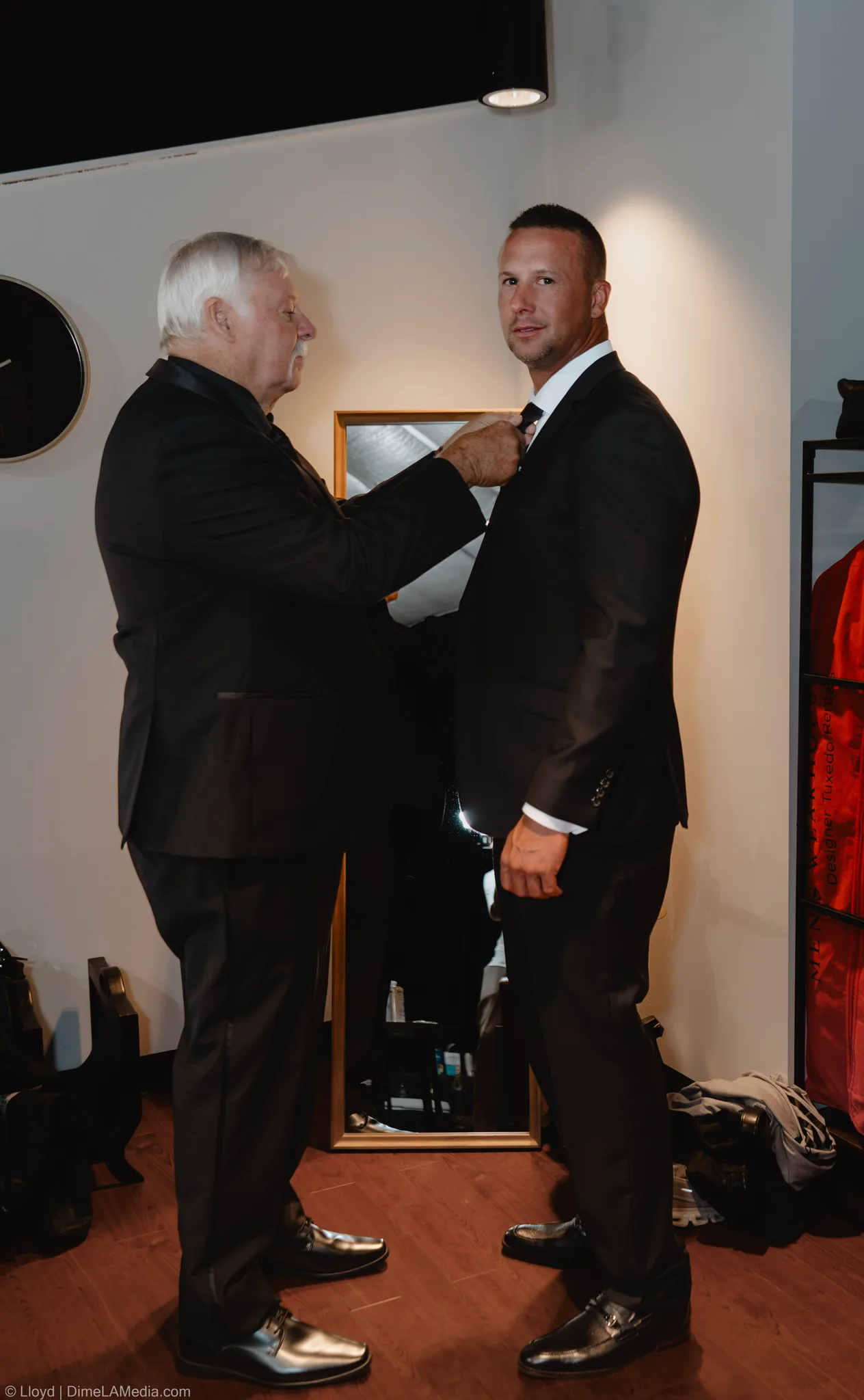 Older man helping the groom with his tie in a warm-lit room
