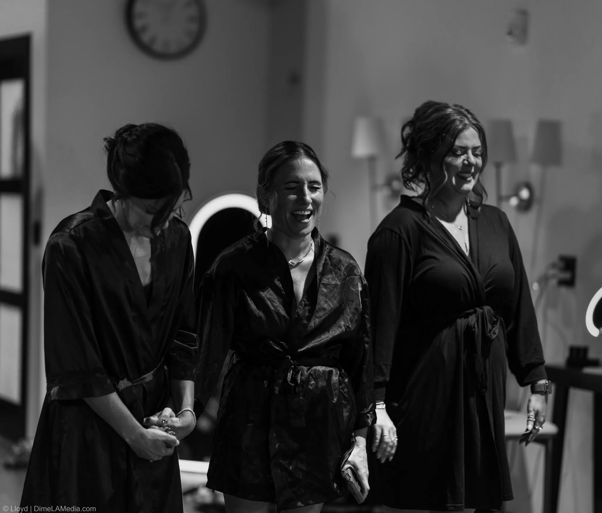 Three bridesmaids in robes laughing together, black and white
