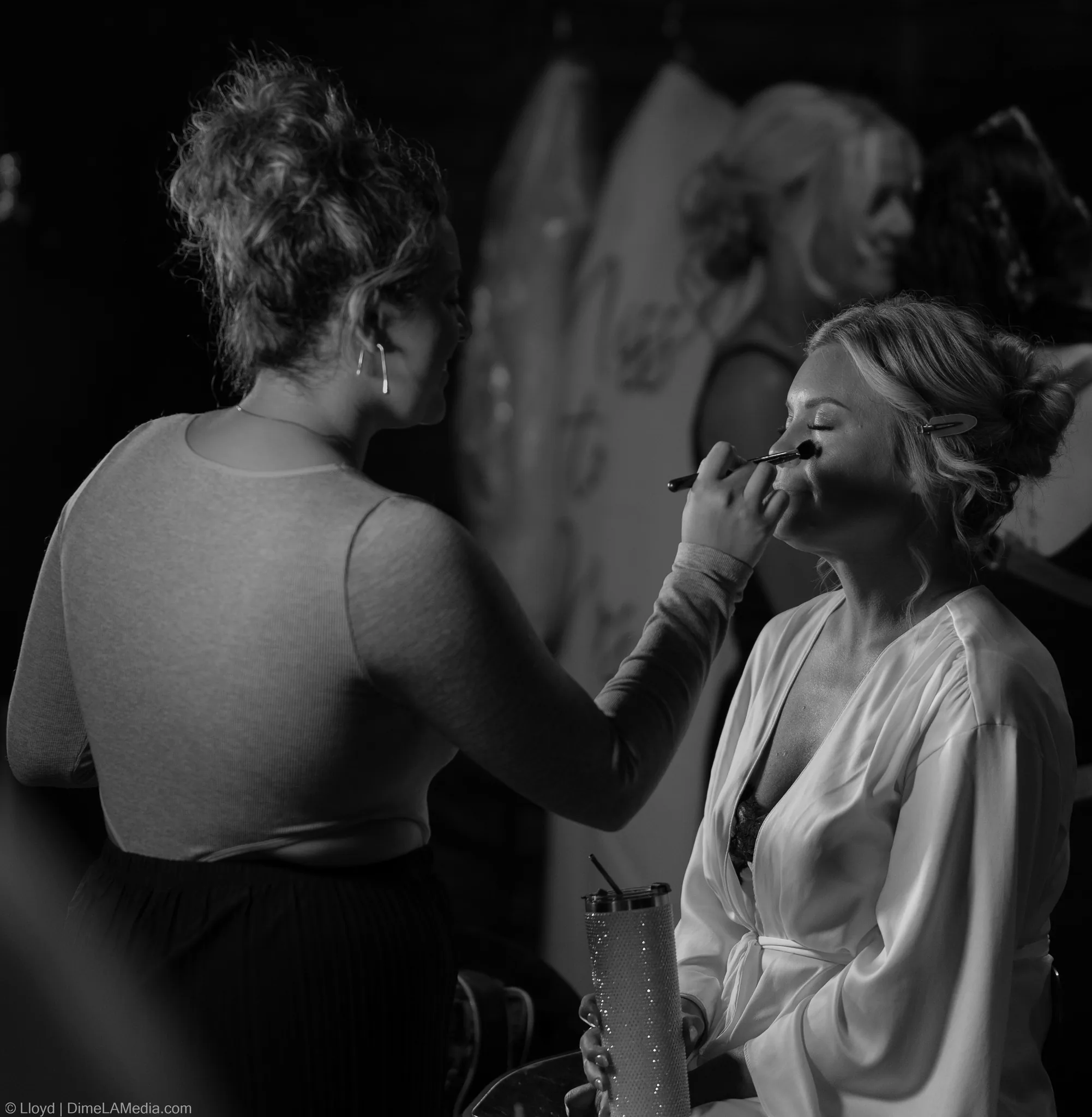 Makeup artist applying a bride's makeup in front of a mirror, black and white