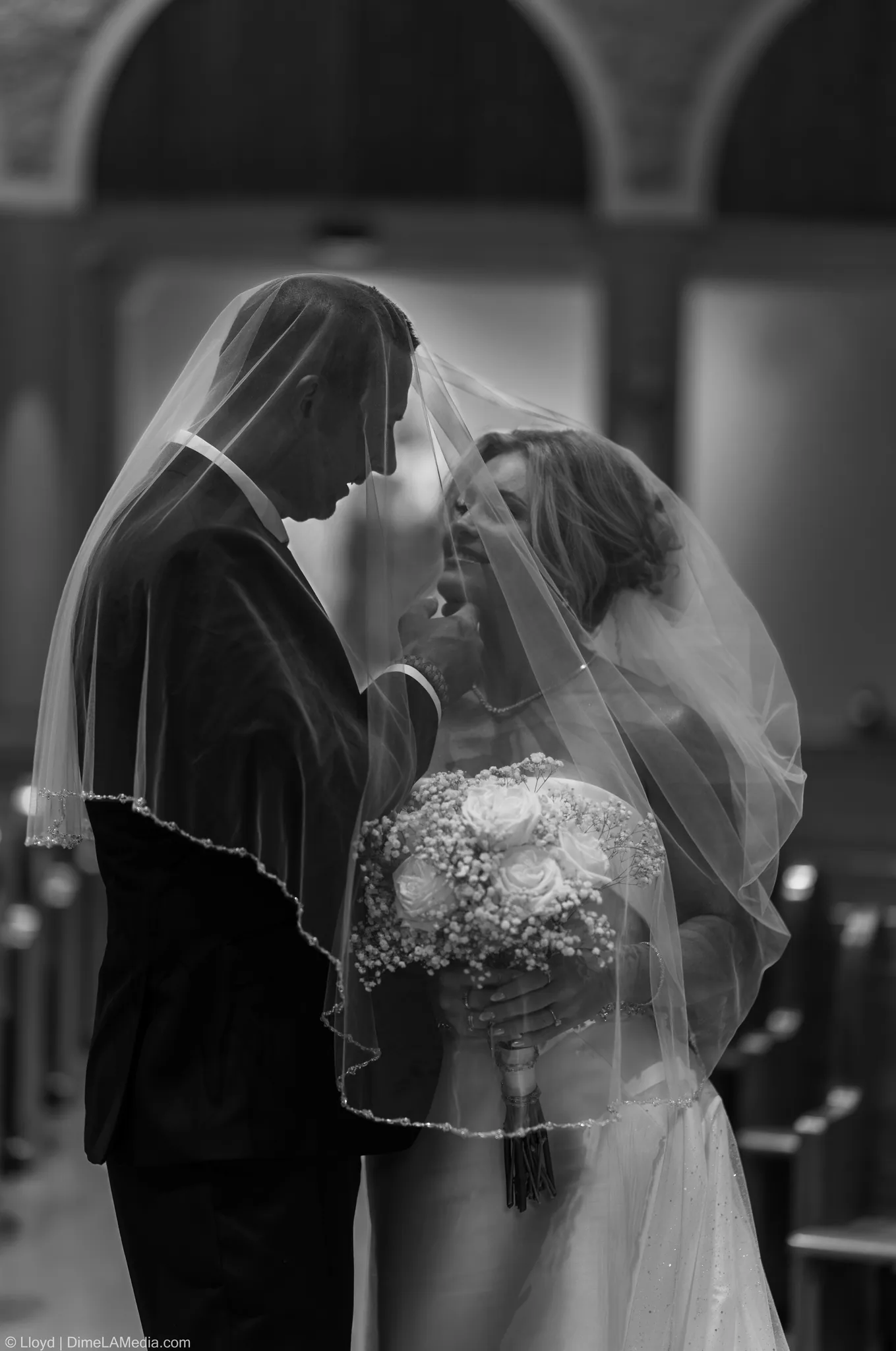 Black and white close frame of the couple under her veil, bouquet in hand