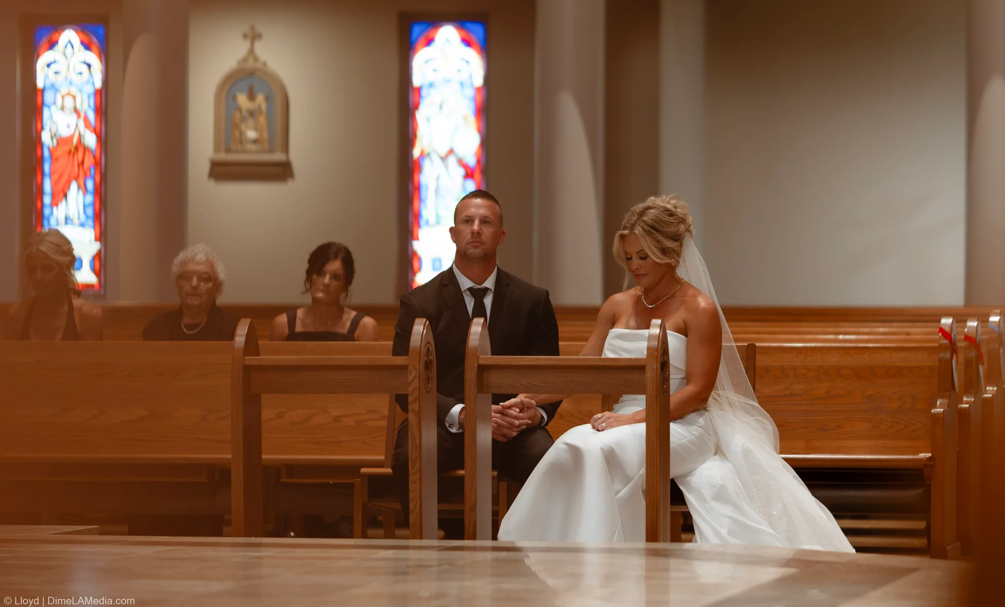 Bride and groom seated in a front pew beneath stained glass windows