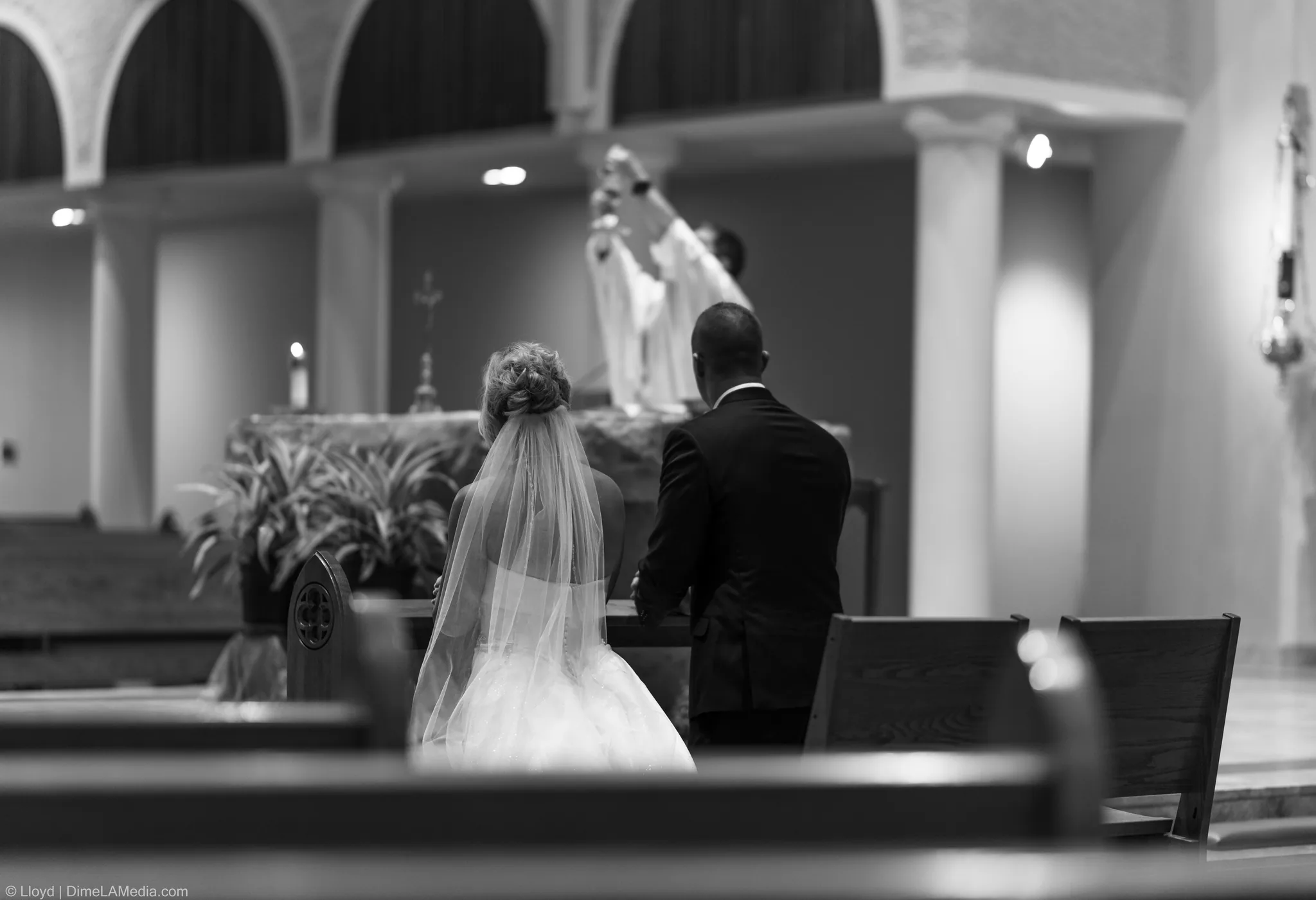 Black and white wide view of the couple at the altar as the priest raises his hands
