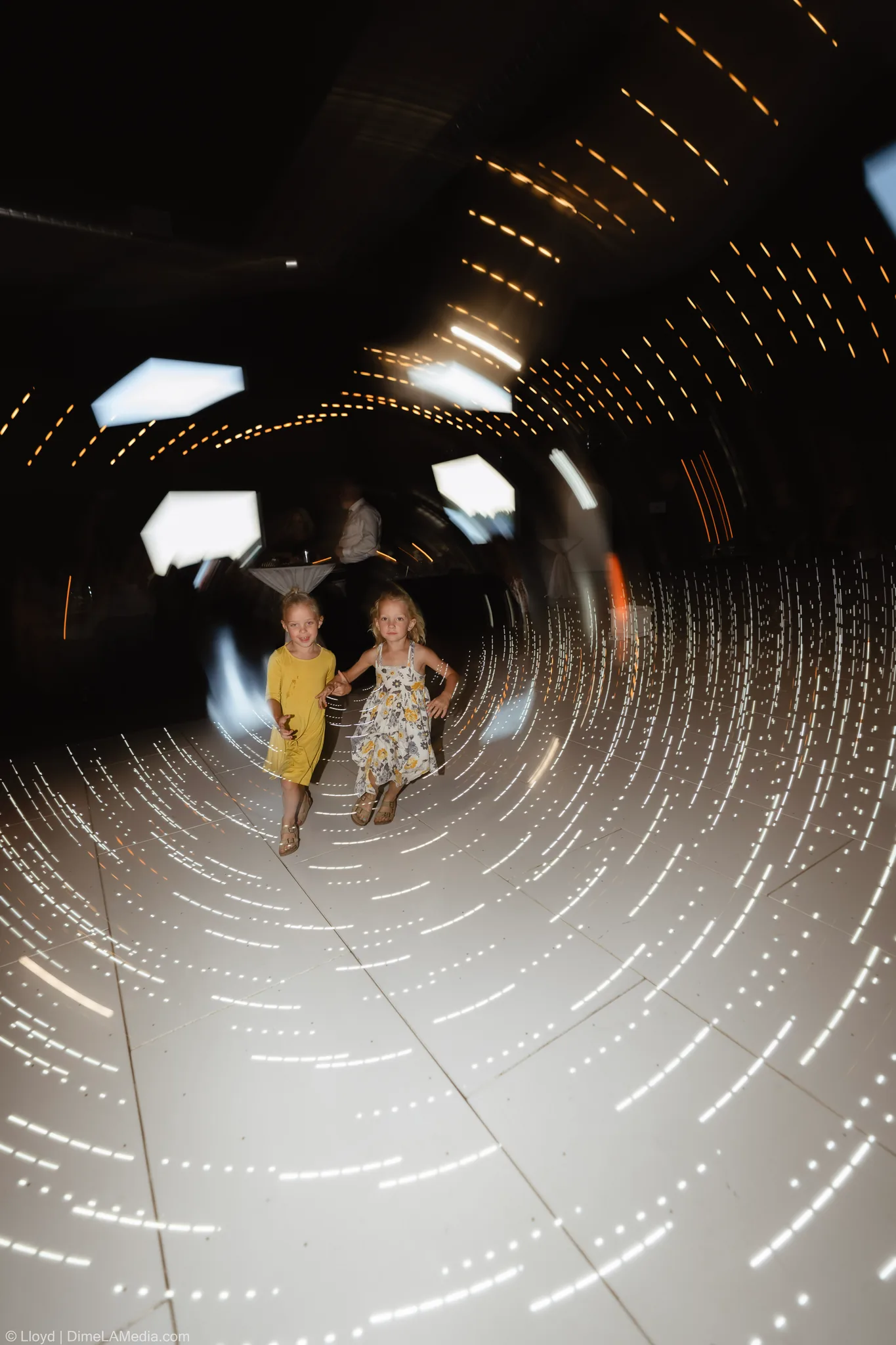 Two young girls running across a light-filled dance floor