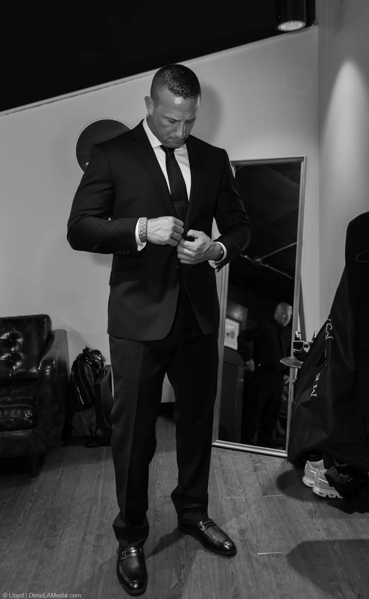 Groom in a dark suit fastening his jacket in front of a mirror