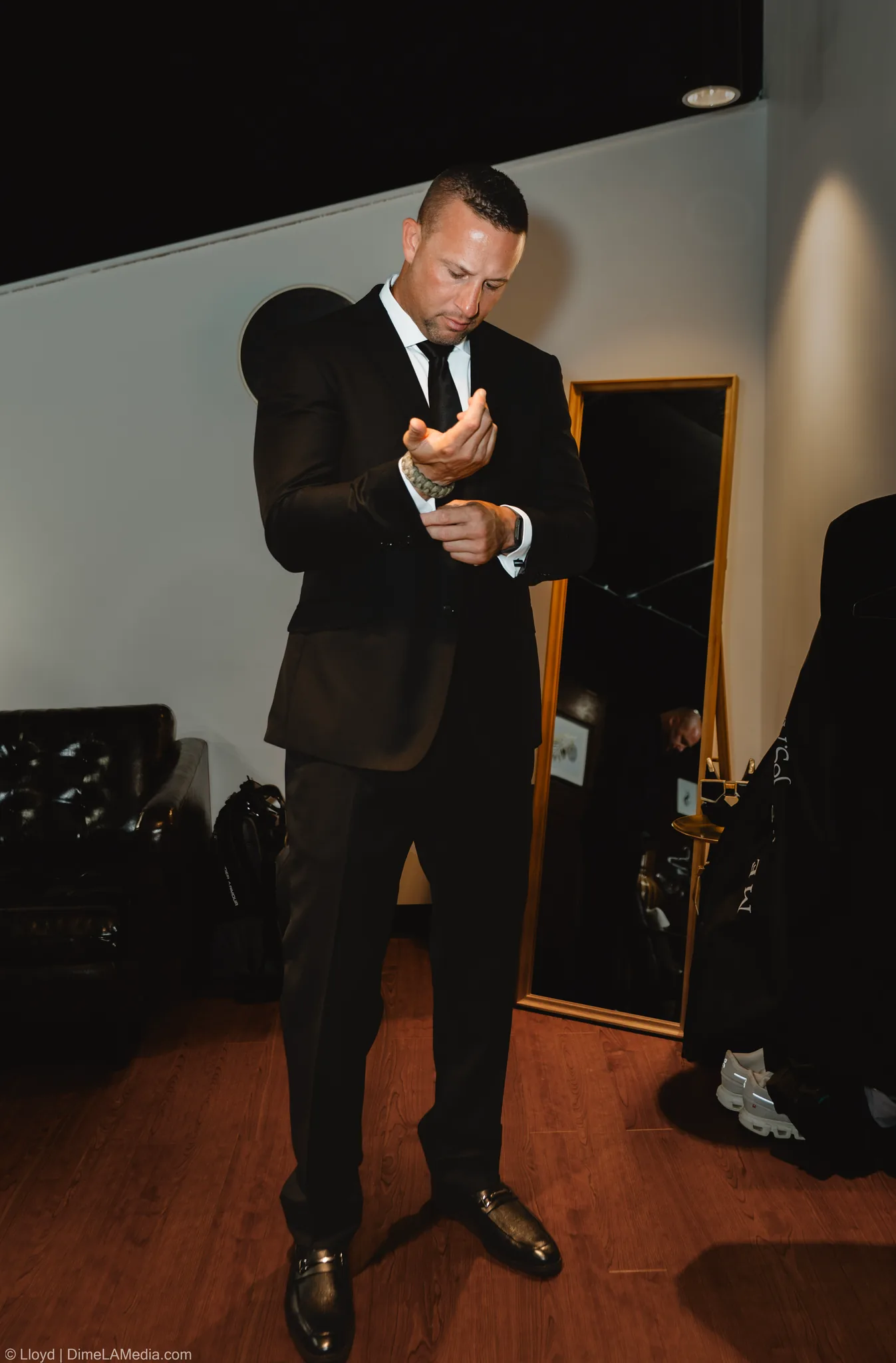 Groom in a dark suit adjusting his cuffs in a mirror-lit room