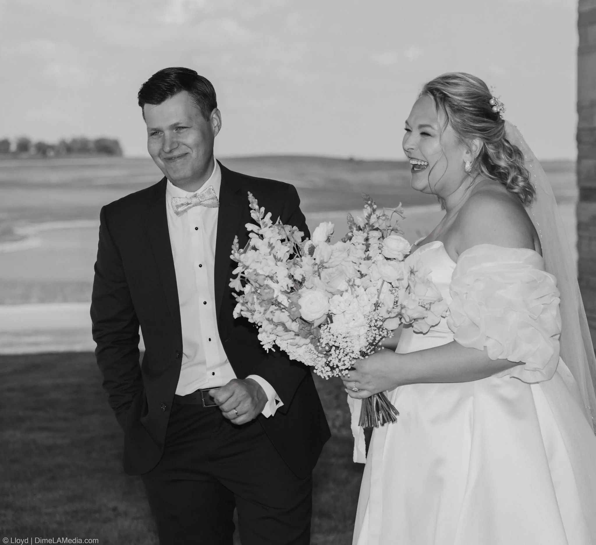 Bride and groom laughing together behind her bouquet, black and white