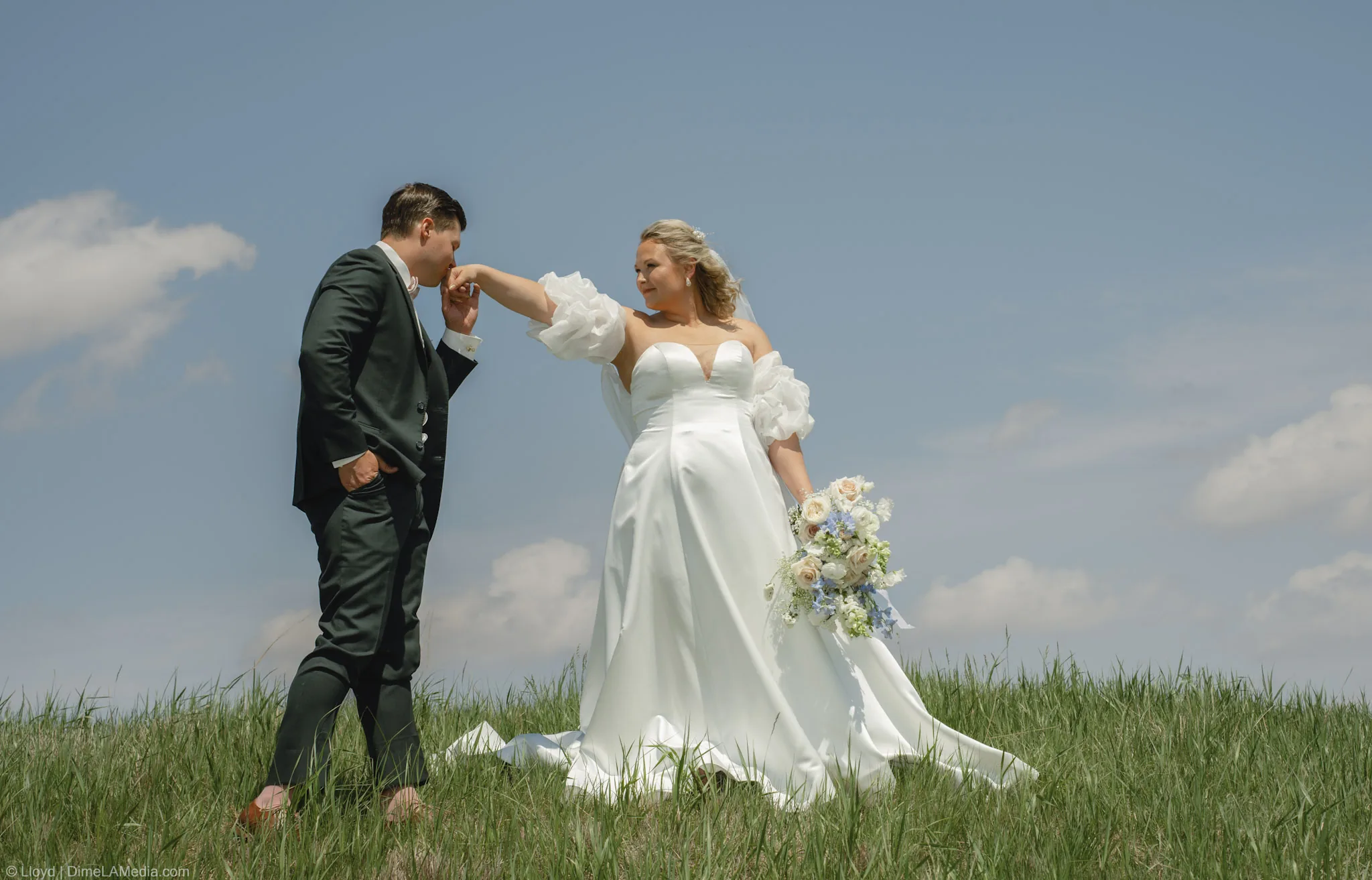 Groom kissing his bride's hand in the tall grass under a wide blue prairie sky, Sioux Falls SD