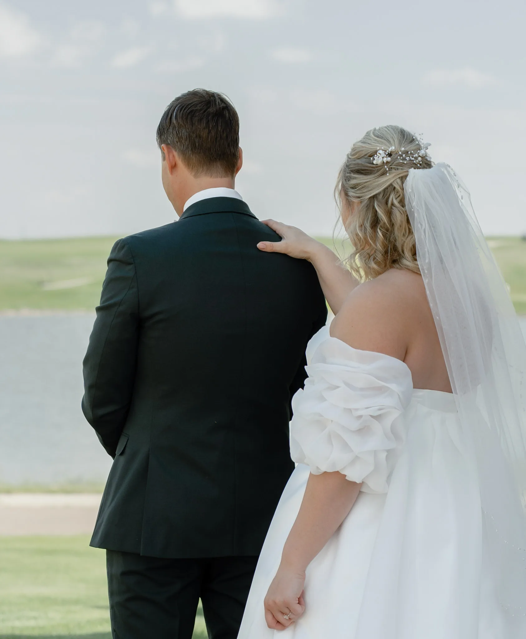 Bride resting a hand on the groom's shoulder the moment before he turns around for their first look