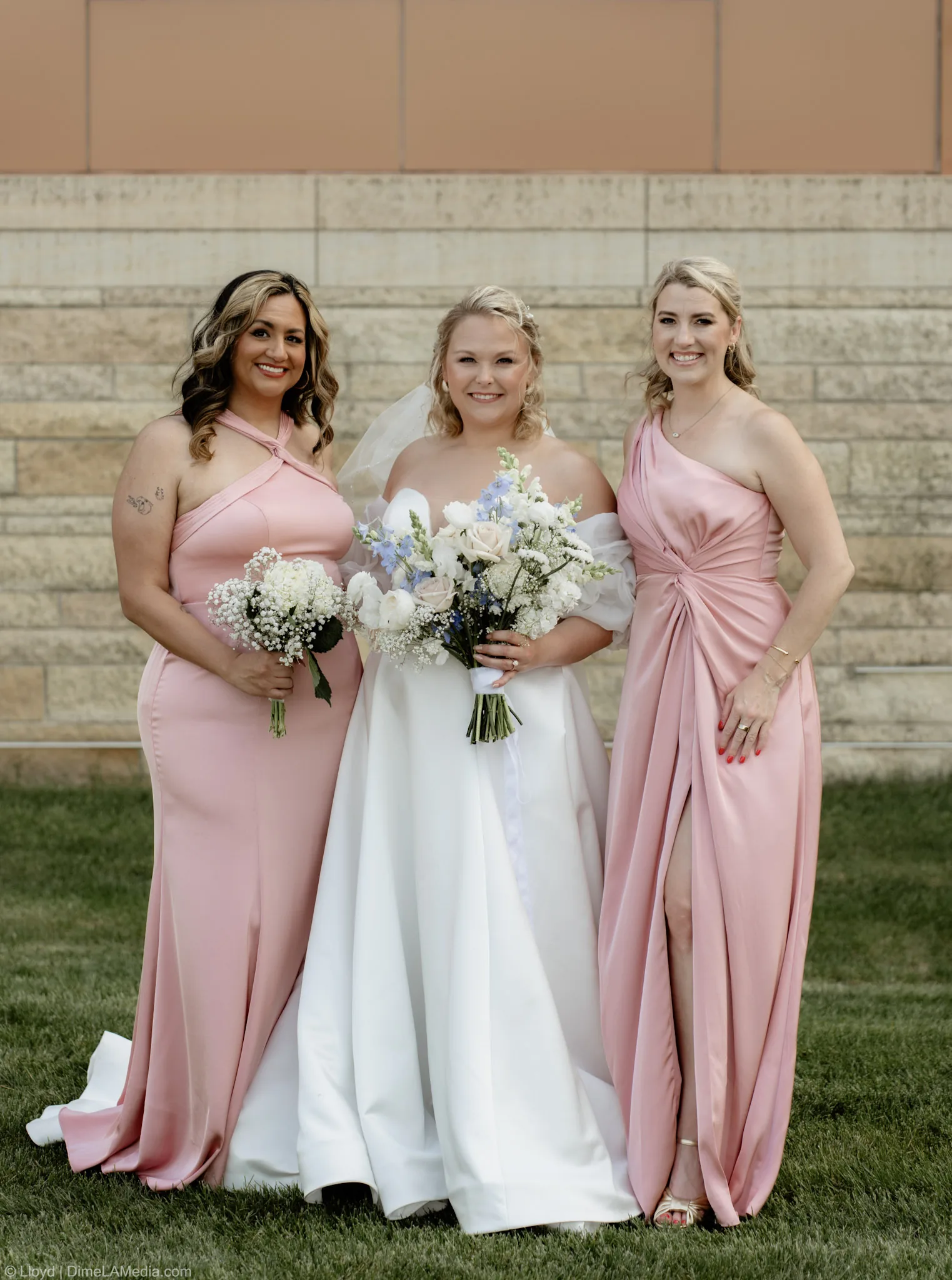 Bride between her two bridesmaids in blush gowns against a limestone wall